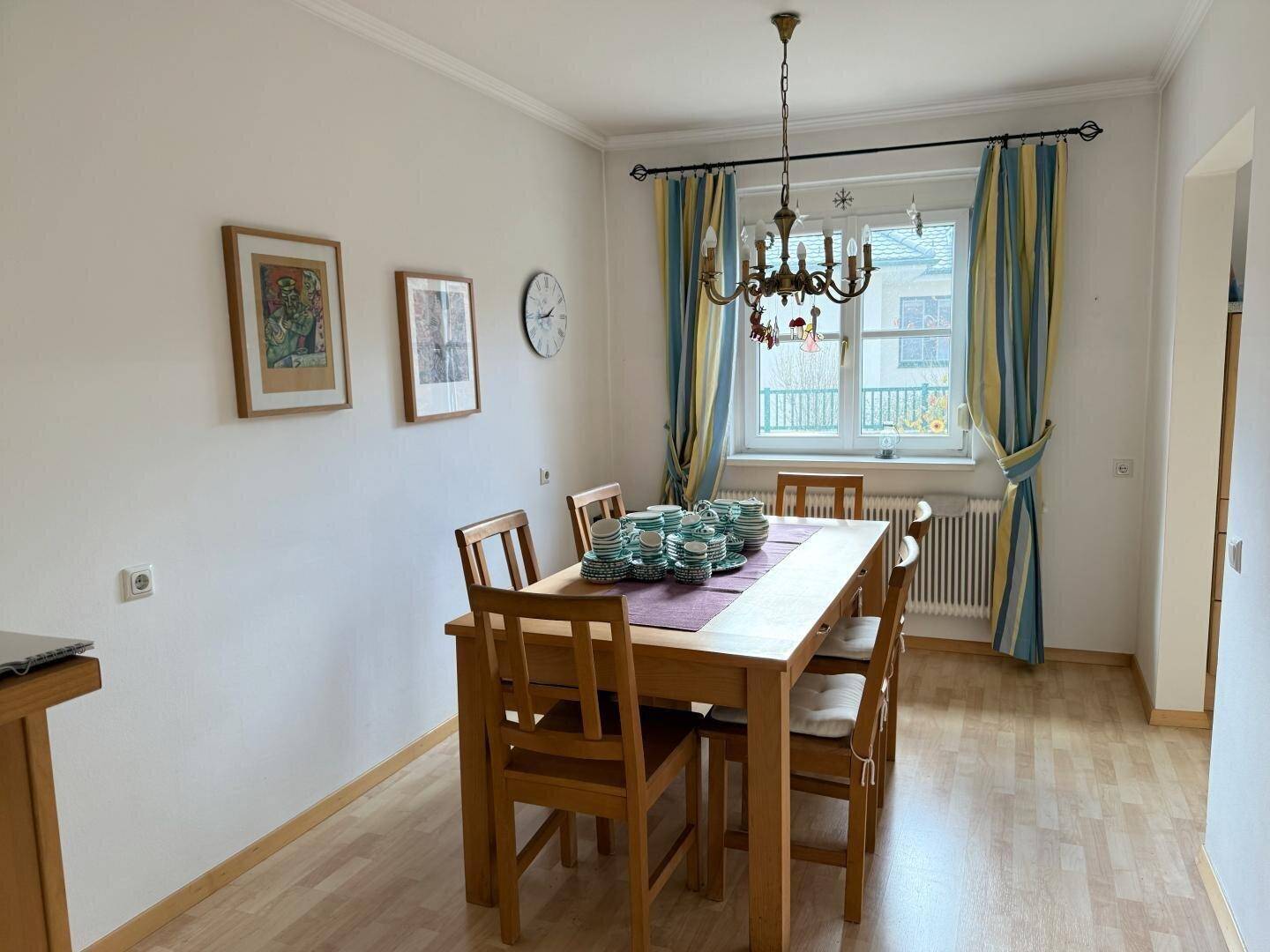 Essbereich mit Holztisch, Stühlen und Fenster mit bunten Vorhängen.