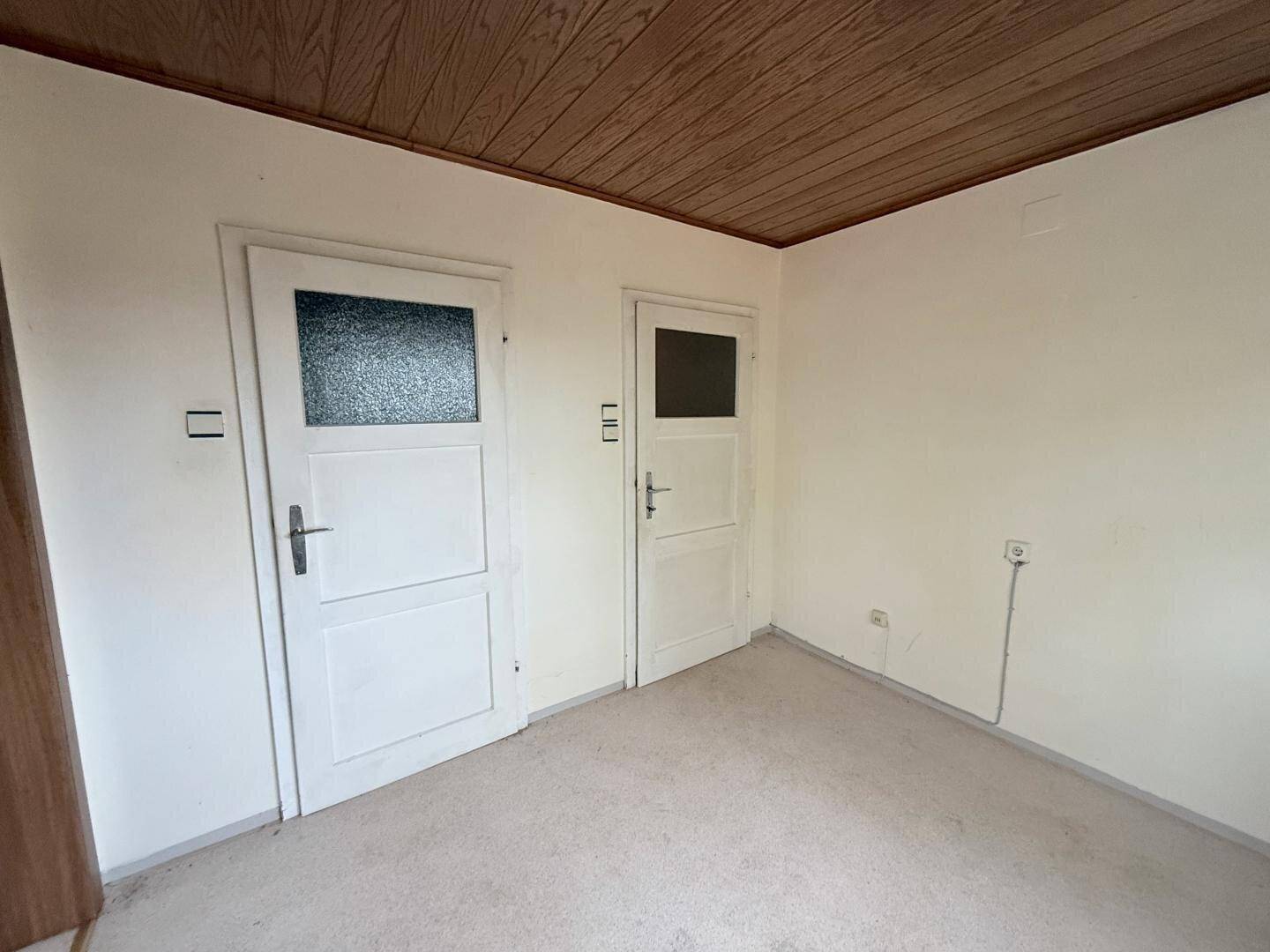 Leerer Raum mit zwei Türen und Holzdecke.