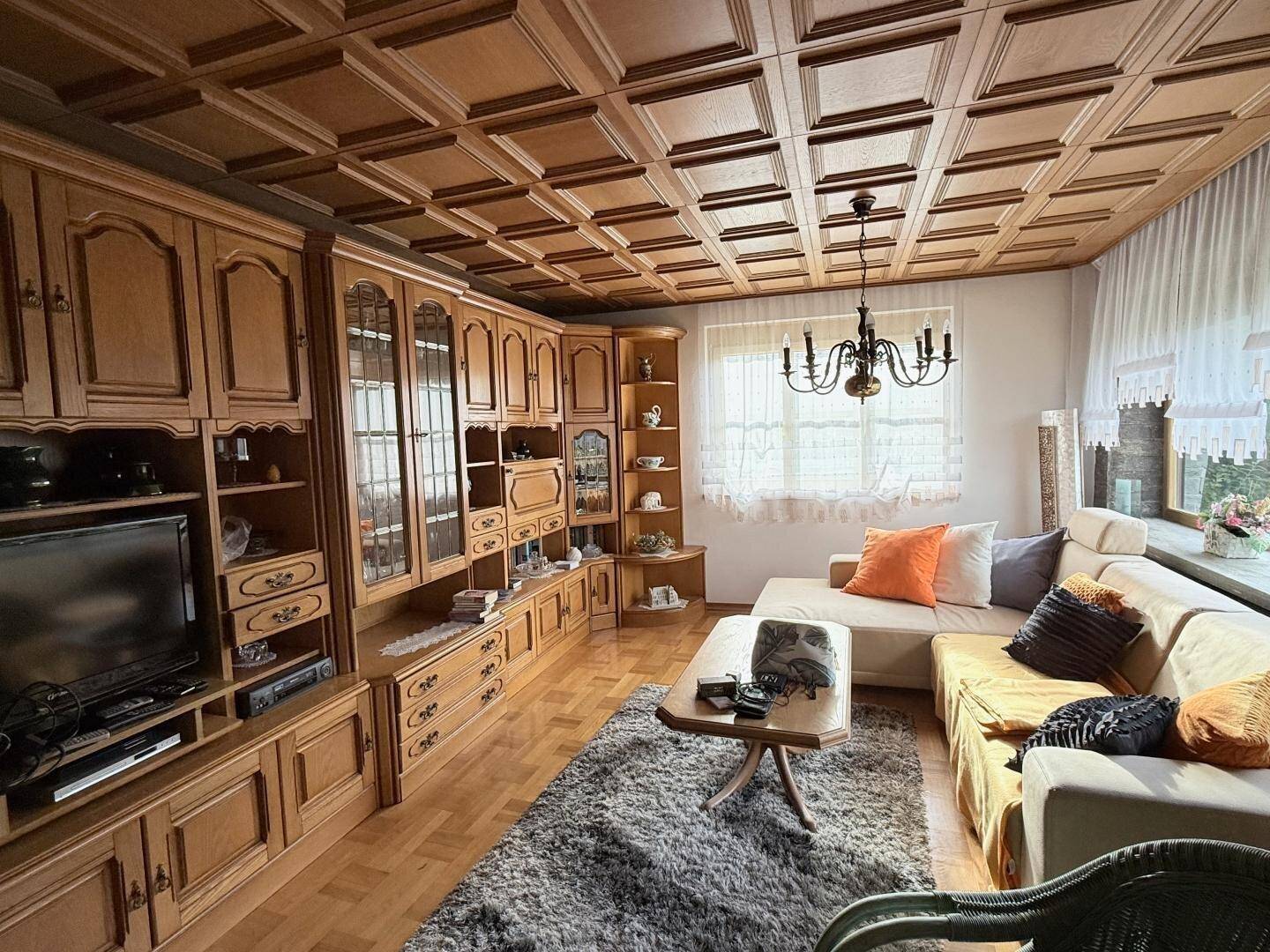 Gemütliches Wohnzimmer mit Holzkassettendecke, großem Sofa und traditionellen Möbeln.
