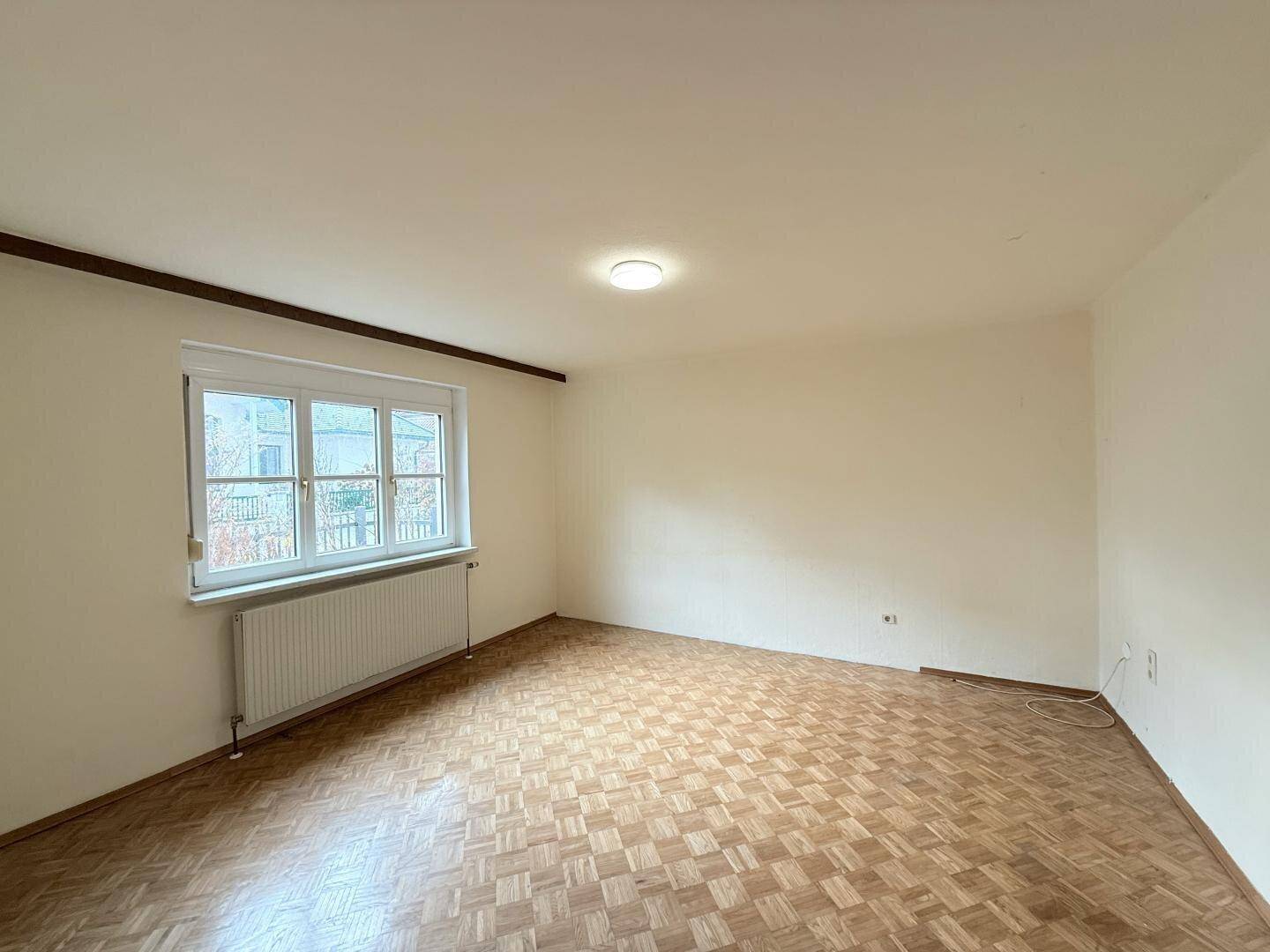 Leerer Wohnraum mit Parkettboden und großem Fenster.