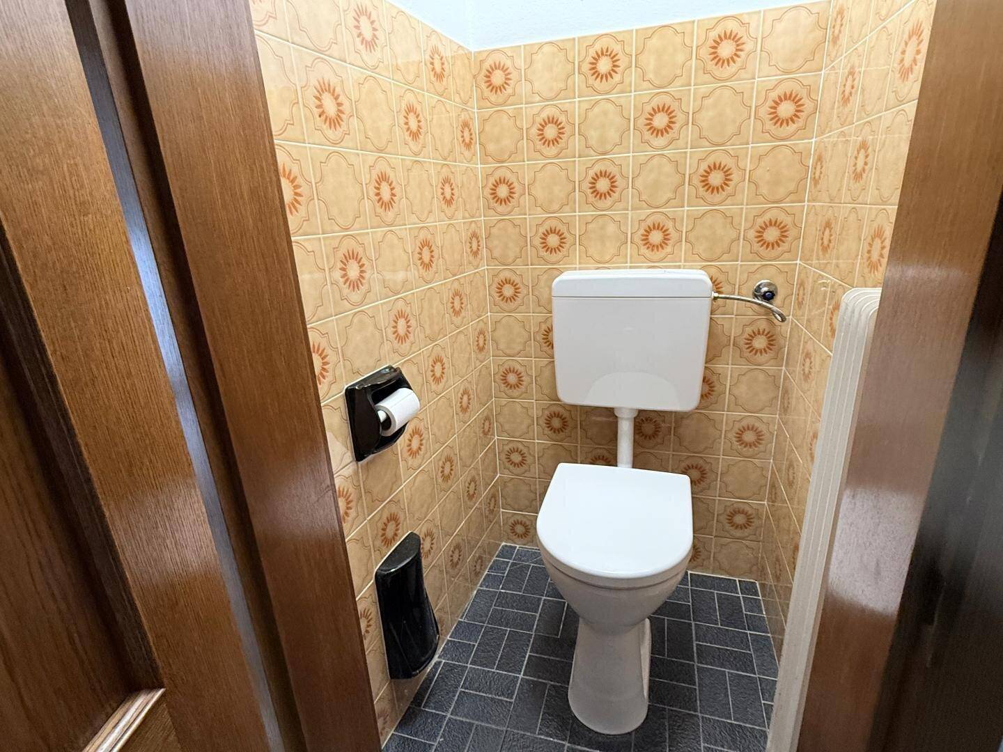 Gäste-WC mit gemusterten Fliesen und wandmontierter Toilette.
