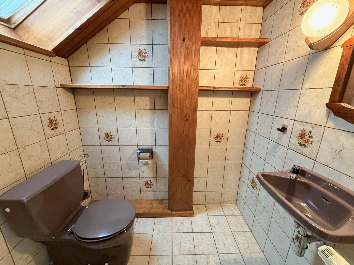 Kleines WC mit gemusterten Fliesen, Bidet und Dachschräge.