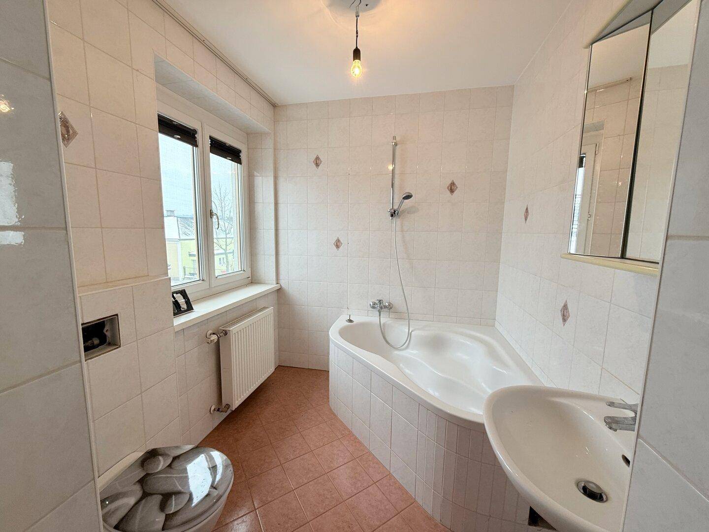 Geräumiges Badezimmer mit Eckbadewanne, Waschbecken und Fenster, hell gefliest und gepflegt.