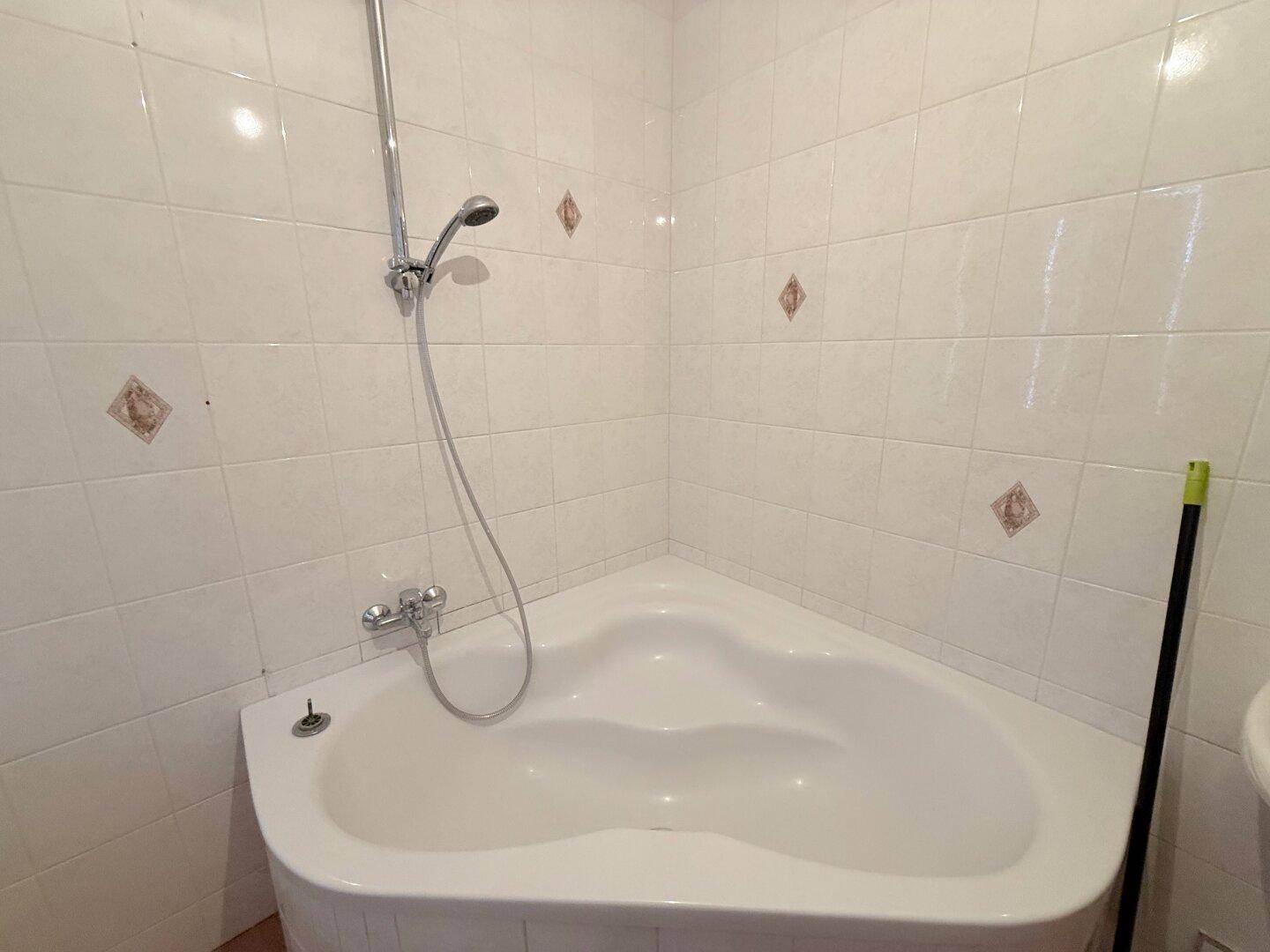 Nahaufnahme einer Eckbadewanne mit Duscharmatur und weißen Fliesen, sauber und funktional.