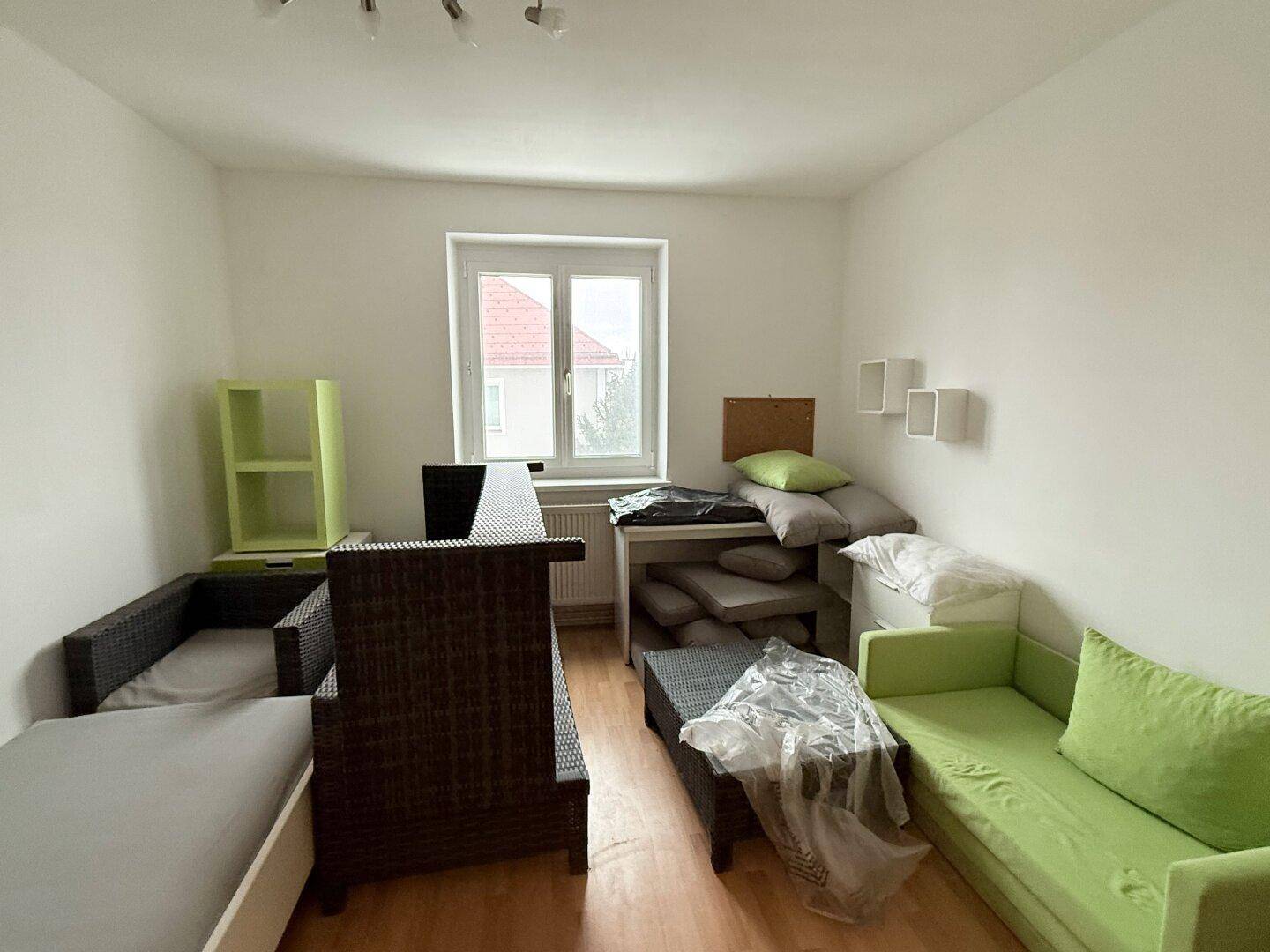 Helles Schlafzimmer mit Holzfußboden, einem Bett und einer grünen Couch, bereit zur Einrichtung.