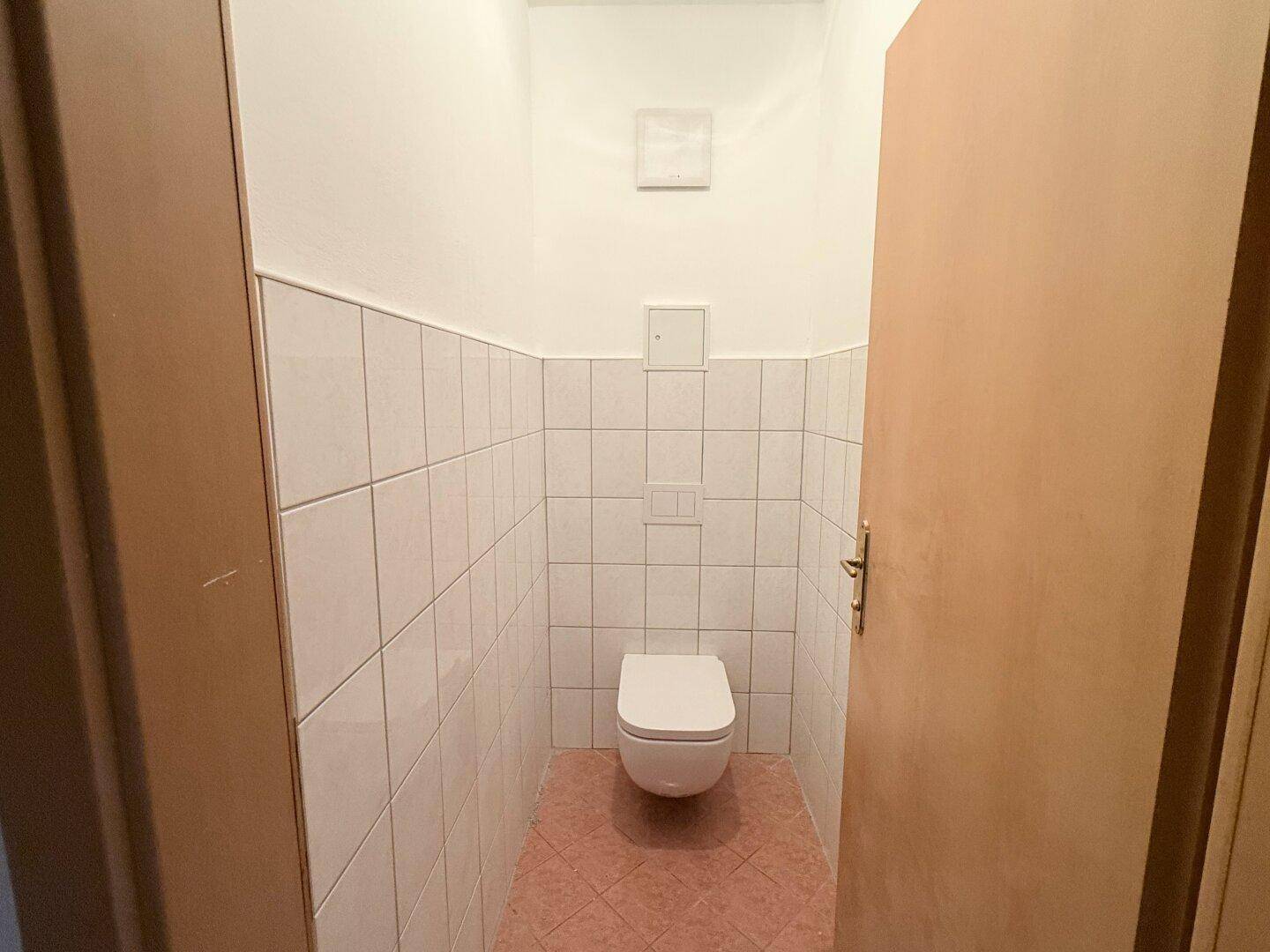 Kleines Gäste-WC mit wandhängender Toilette und weißen Fliesen an den Wänden, funktional und sauber.