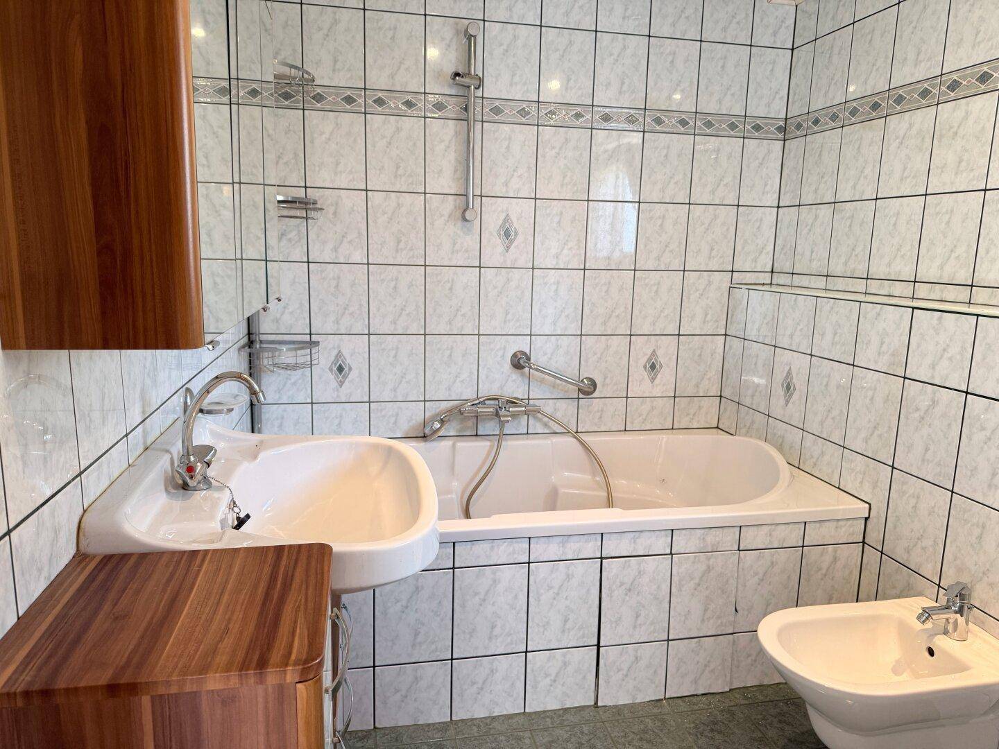 Helles Badezimmer mit Badewanne, Bidet, Duschfunktion und Haltegriffen an der Wand.