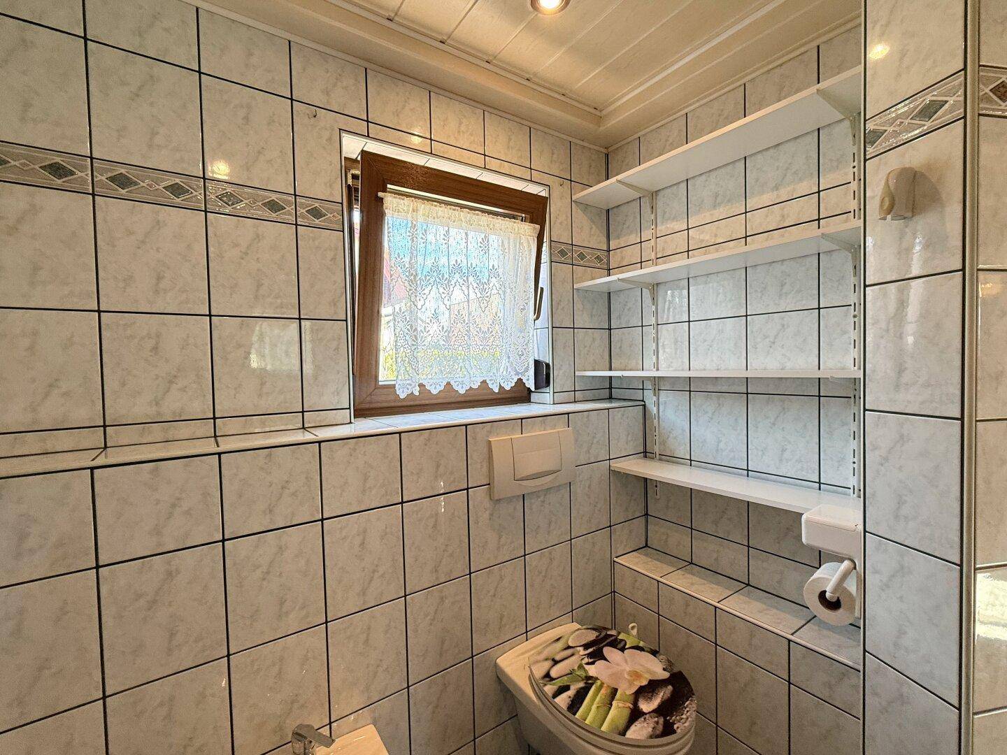 Kleines WC mit Fenster, Wandregalen und einem dekorativen Toilettensitz.