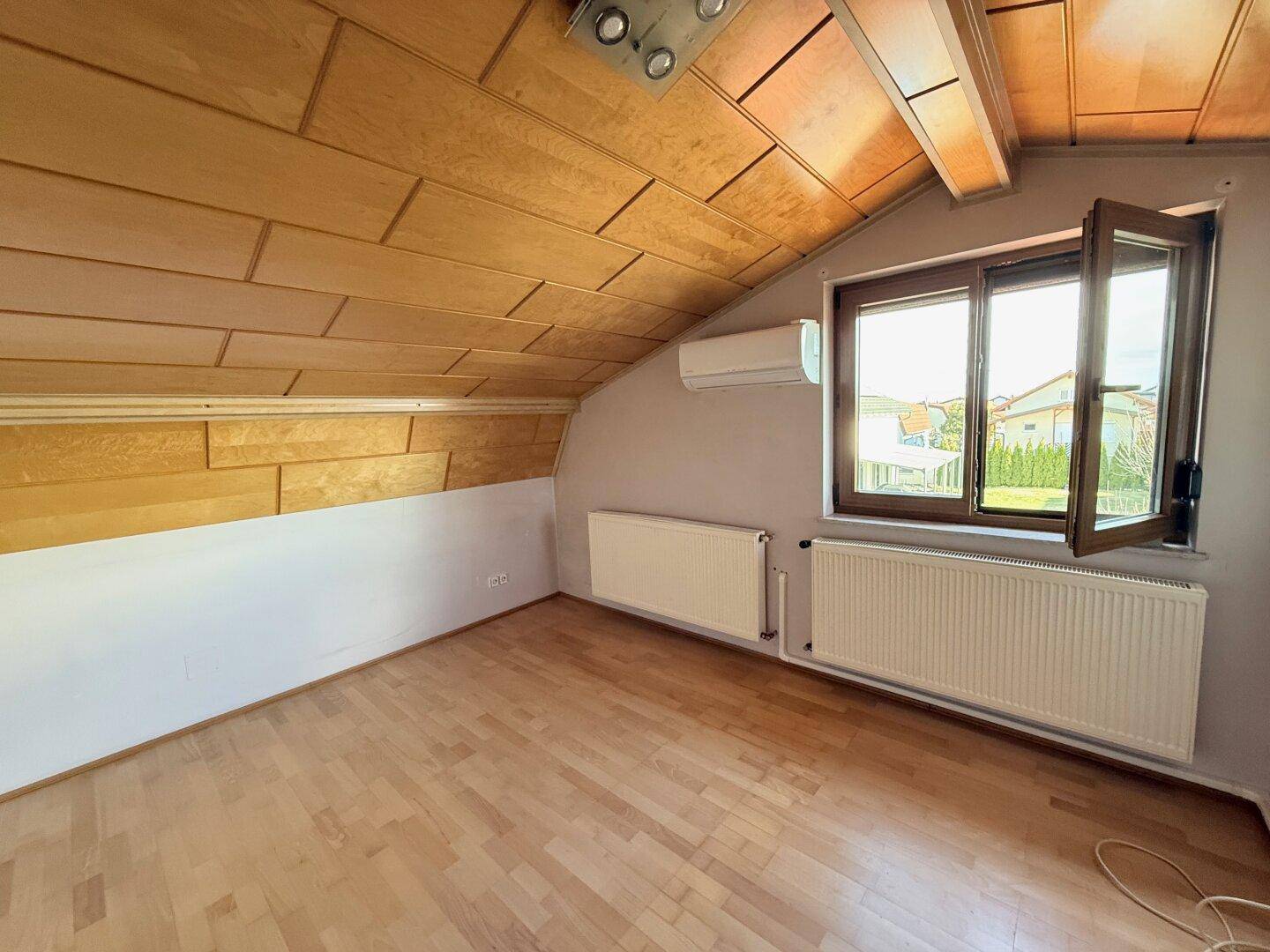 Helles Zimmer im Dachgeschoss mit Holzboden, Dachschräge und Klimaanlage.