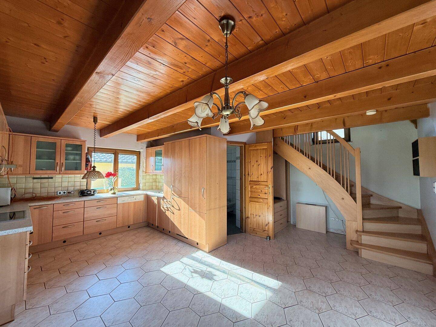 Offener Wohnbereich mit Holzküche, sichtbaren Balken und einer Holztreppe zum Obergeschoss.