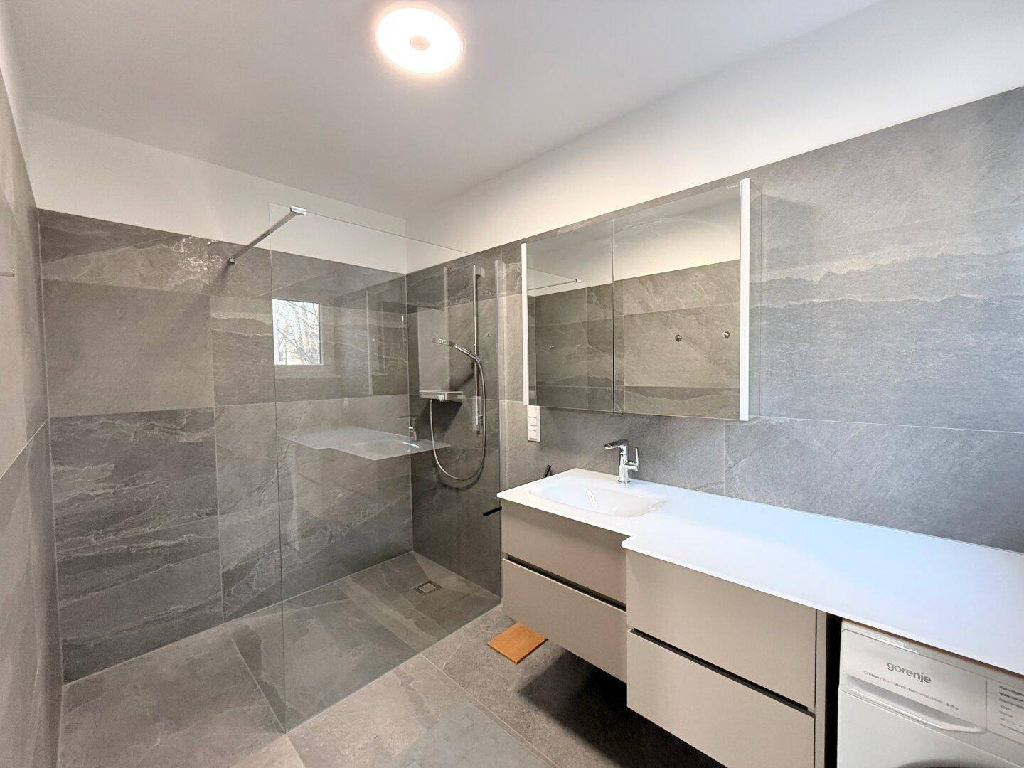 Geräumiges Badezimmer mit großer begehbarer Dusche, Waschbecken und Waschmaschine.