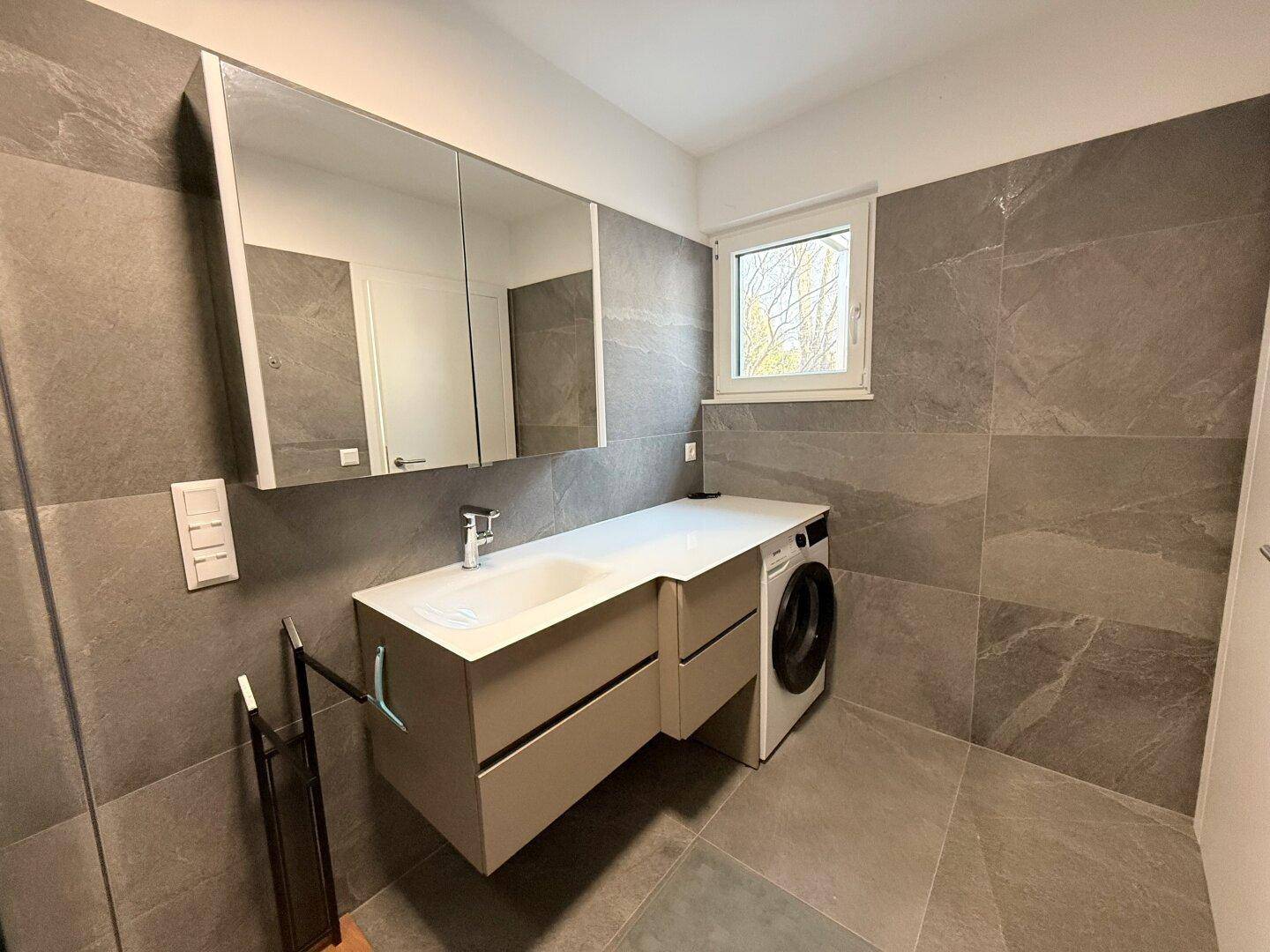 Modernes Badezimmer mit Waschbecken, Spiegelschrank, Waschmaschine und Fenster.