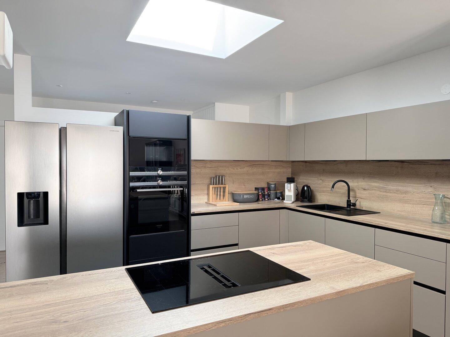 Moderne Küche mit Kücheninsel, Induktionskochfeld und integrierten Geräten unter einem Dachfenster.