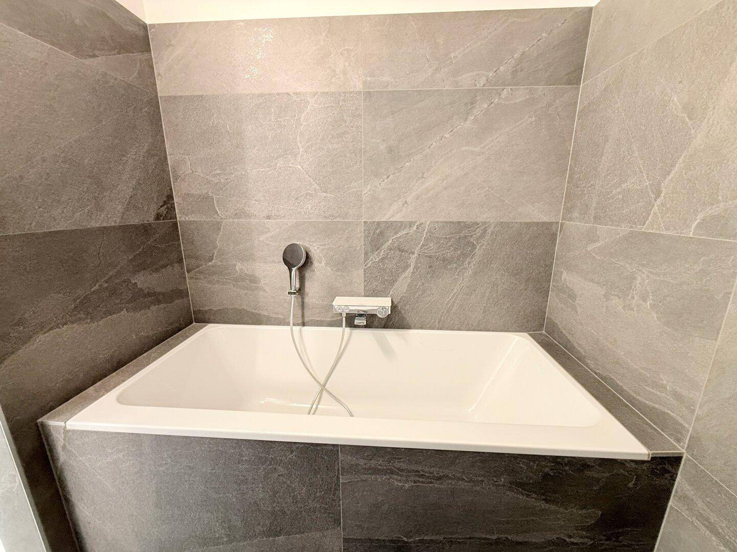 Eingebaute Badewanne mit grauen Fliesen in einem modernen Badezimmer.