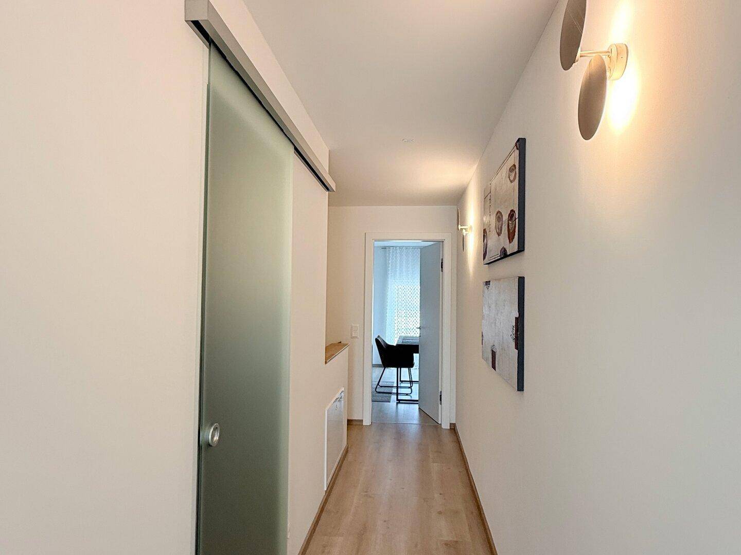 Heller Flur mit Schiebetür aus Glas und Blick in ein weiteres Zimmer.
