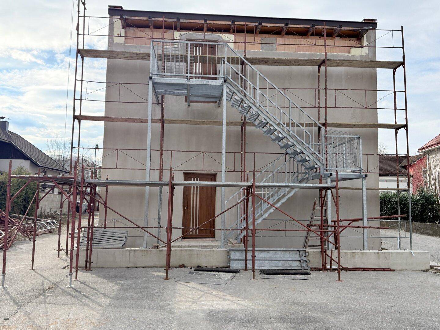 Rohbau eines Gebäudes mit Gerüst und provisorischer Außentreppe, bereit für den weiteren Ausbau.