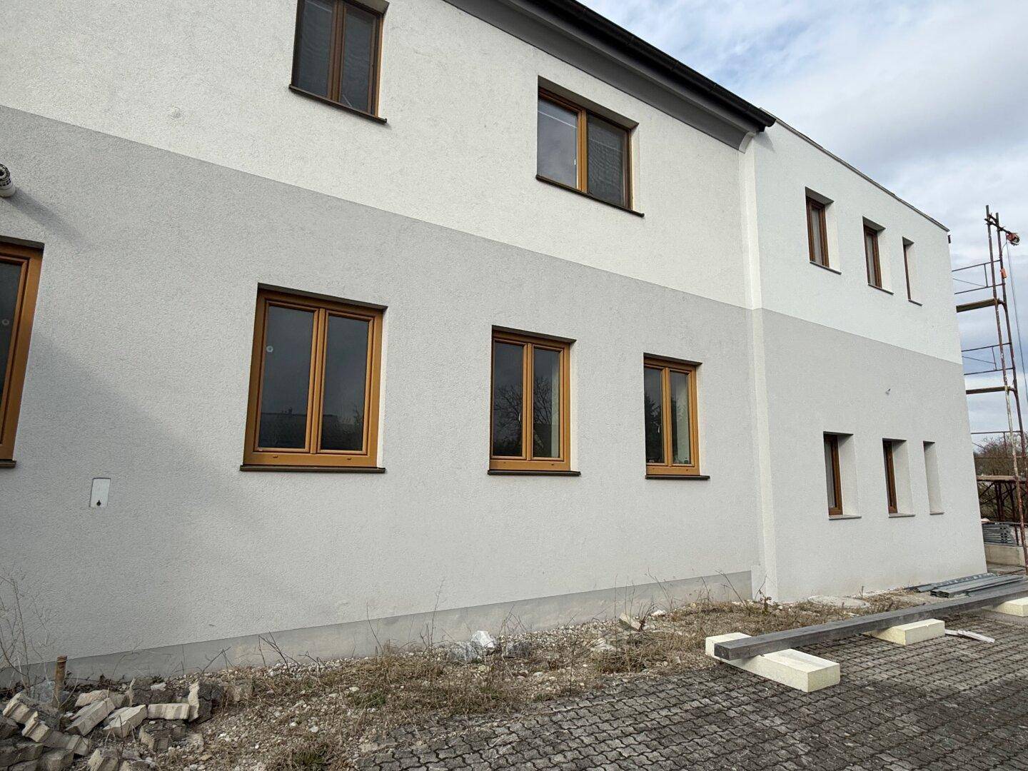 Fassade eines Neubaus mit zweifarbigem Putz und neuen Holzfenstern, teilweise noch im Bau.