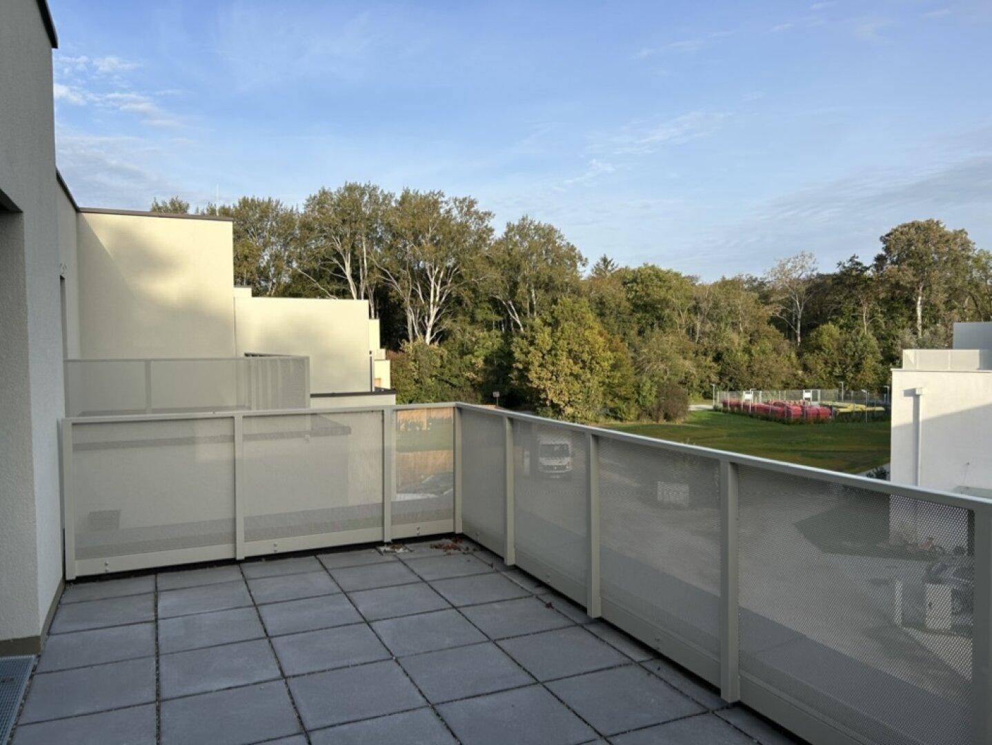 Dachterrasse mit grauen Fliesen, moderner Brüstung und Blick ins Grüne.