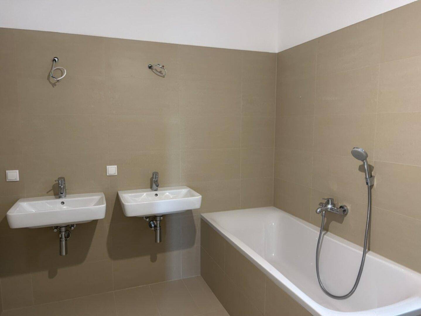 Badezimmer mit zwei Waschbecken und einer Badewanne, hell gefliest.