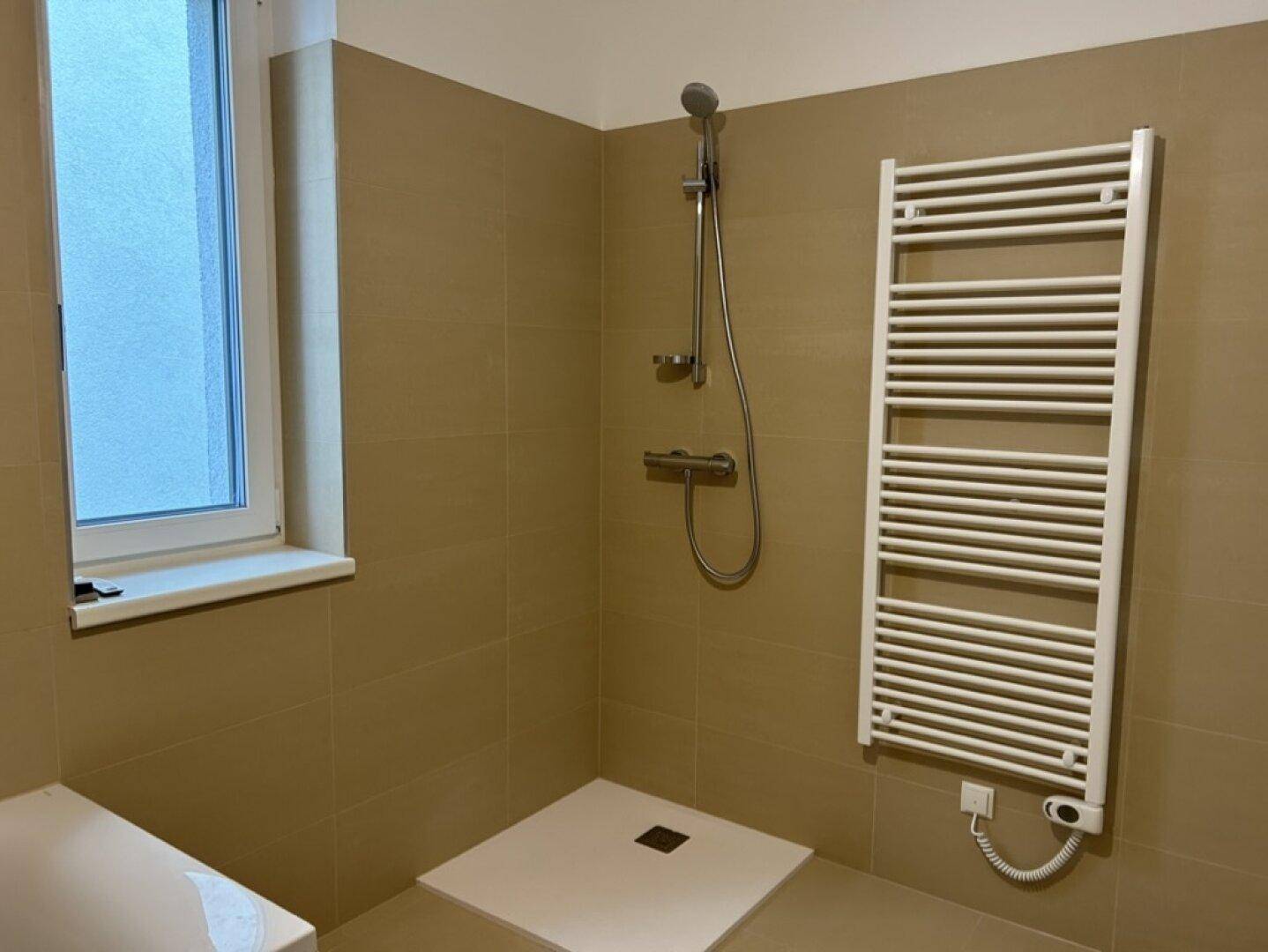 Badezimmer mit Duschbereich, beheiztem Handtuchhalter und Fenster.