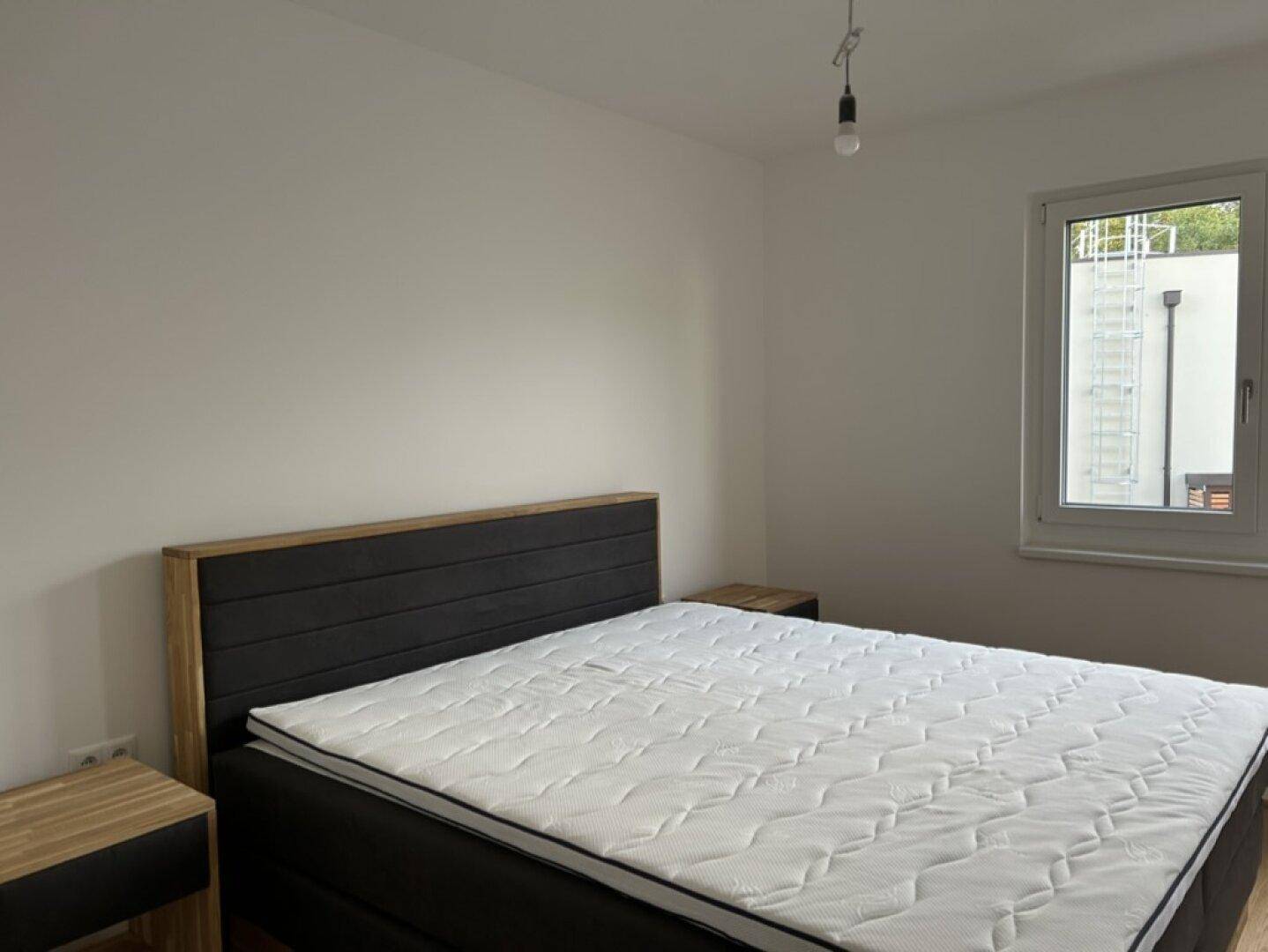 Schlafzimmer mit Bett, Nachttischen aus Holz und einem Fenster.