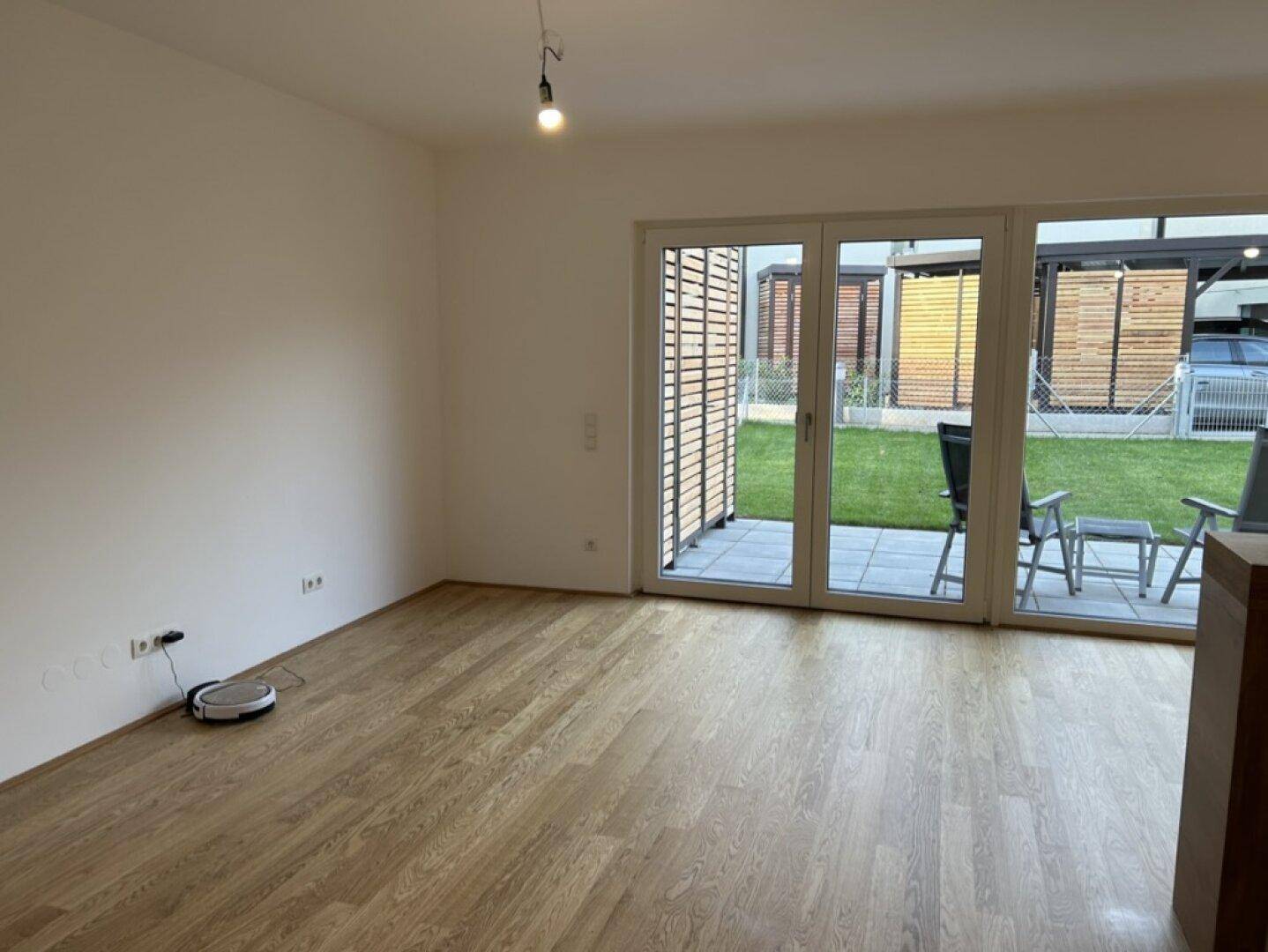 Wohnzimmer mit Holzboden, weißen Wänden und großem Zugang zum Garten.