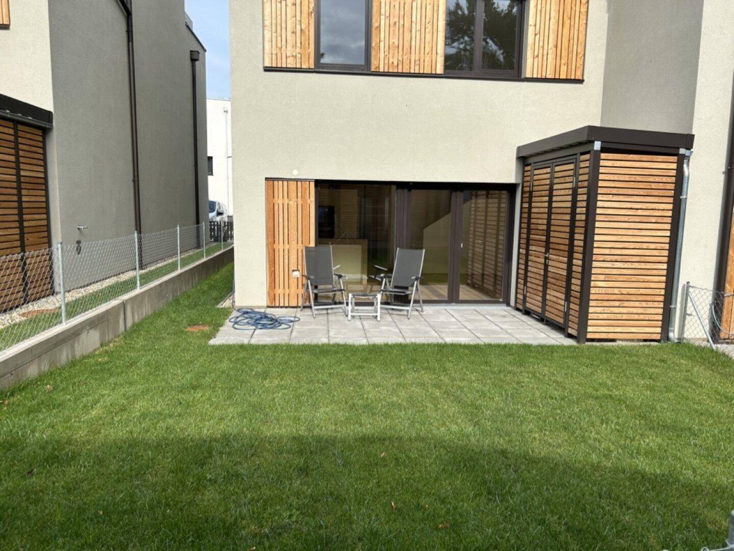 Kleiner Gartenbereich mit Rasenfläche, gepflasterter Terrasse und Sitzgelegenheiten.