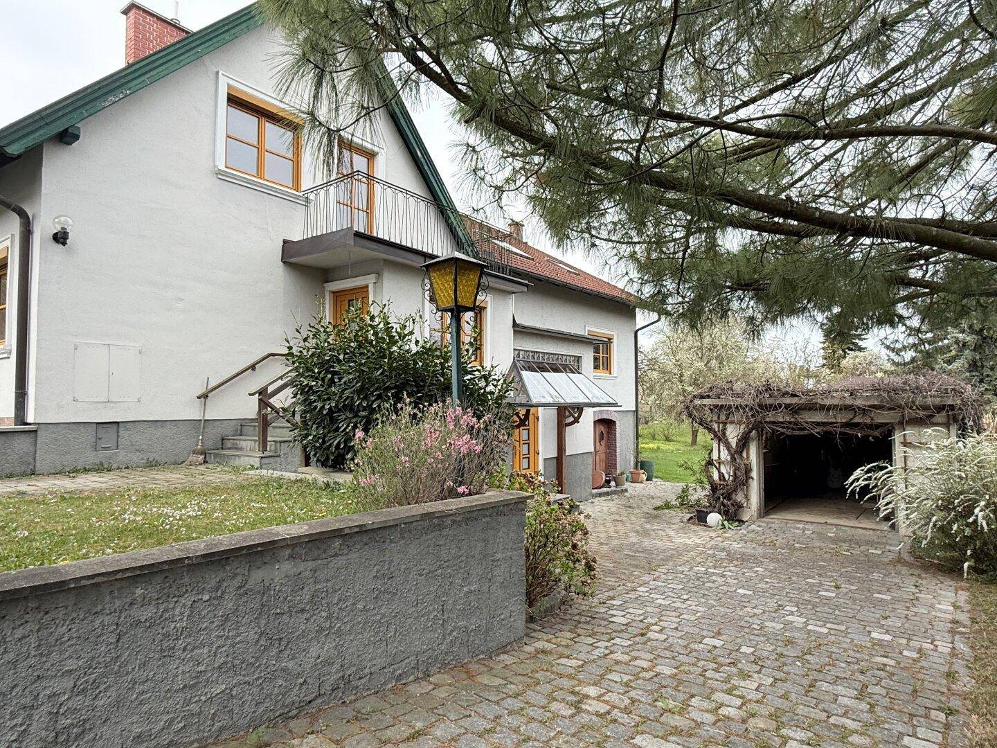 Seitenansicht des Hauses mit gepflasterter Auffahrt, Carport und einem kleinen Balkon.