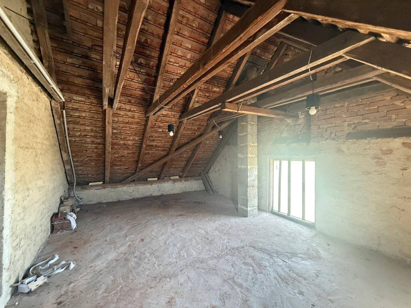 Unausgebauter Dachboden mit sichtbaren Holzbalken und Ziegelwänden, bereit für den Ausbau.