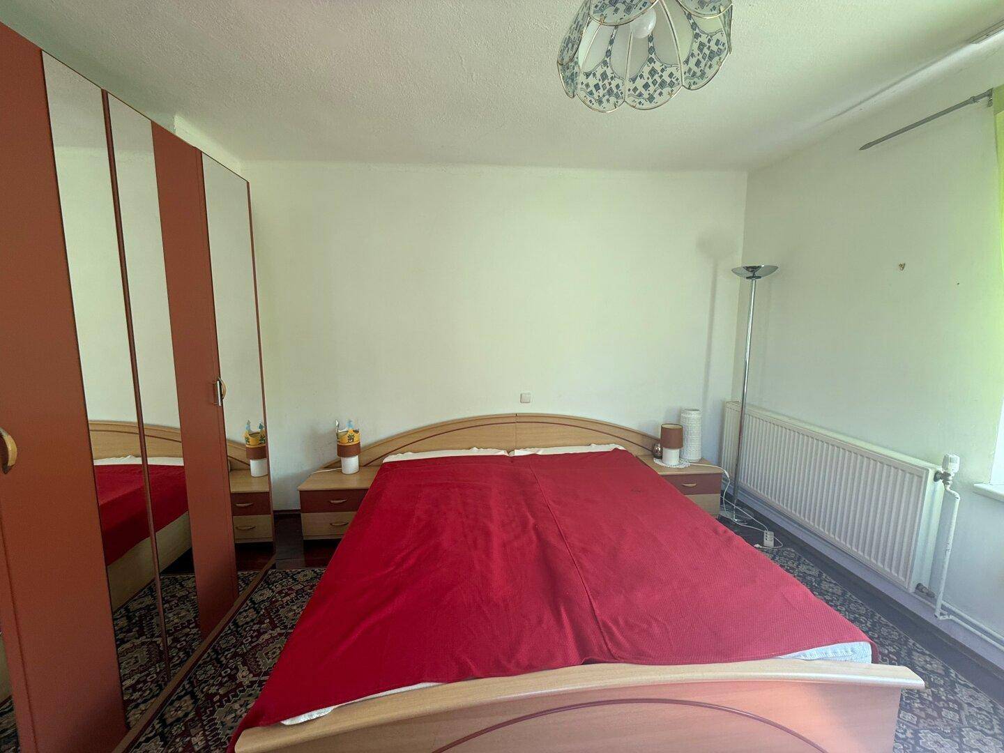 Schlafzimmer mit Doppelbett, großem Spiegelschrank und einem Heizkörper unter dem Fenster.