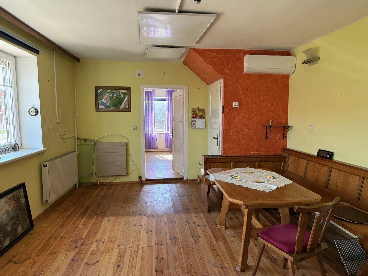 Gemütliches Wohnzimmer mit Holzboden, einer Eckbank und farbigen Wänden in Gelb und Orange.