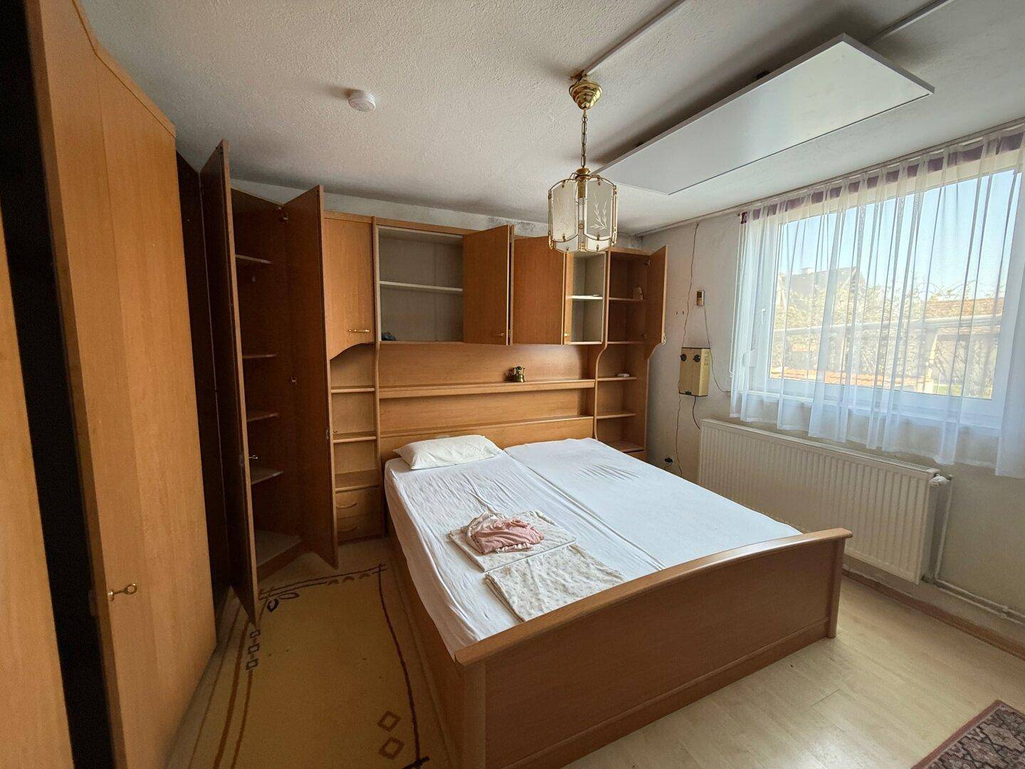 Schlafzimmer mit Holzmöbeln, integriertem Bett und einem Fenster, das Tageslicht hereinlässt.
