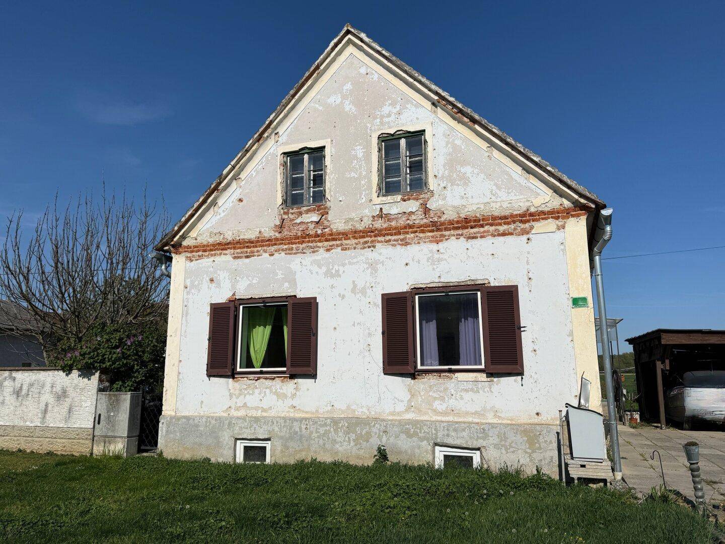 Alte Hausfassade mit abblätterndem Putz, traditionellen Fenstern und braunen Fensterläden.