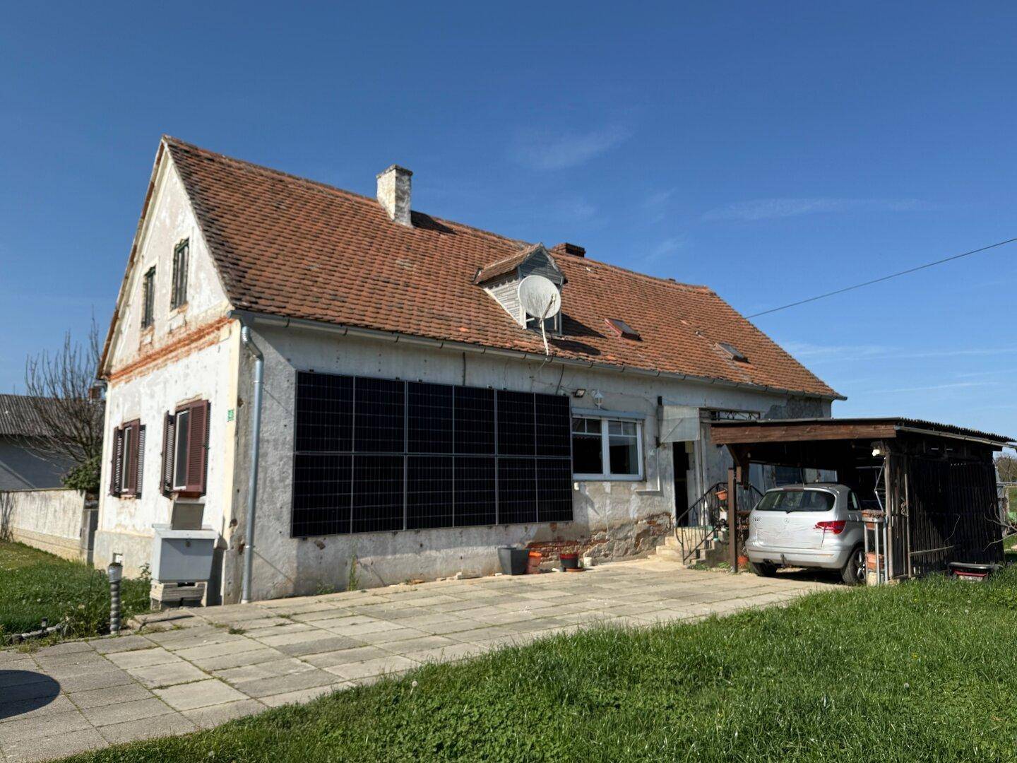 Seitenansicht des Hauses mit Photovoltaikmodulen an der Wand und einem Carport für Fahrzeuge.