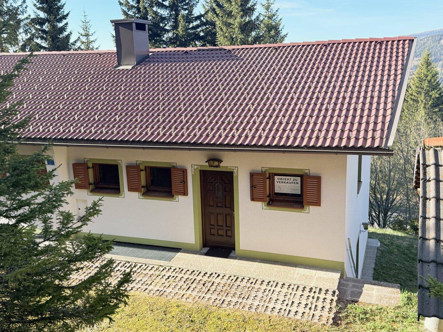 Traditionelles Haus mit Satteldach, Holzfensterläden und grüner Umgebung.