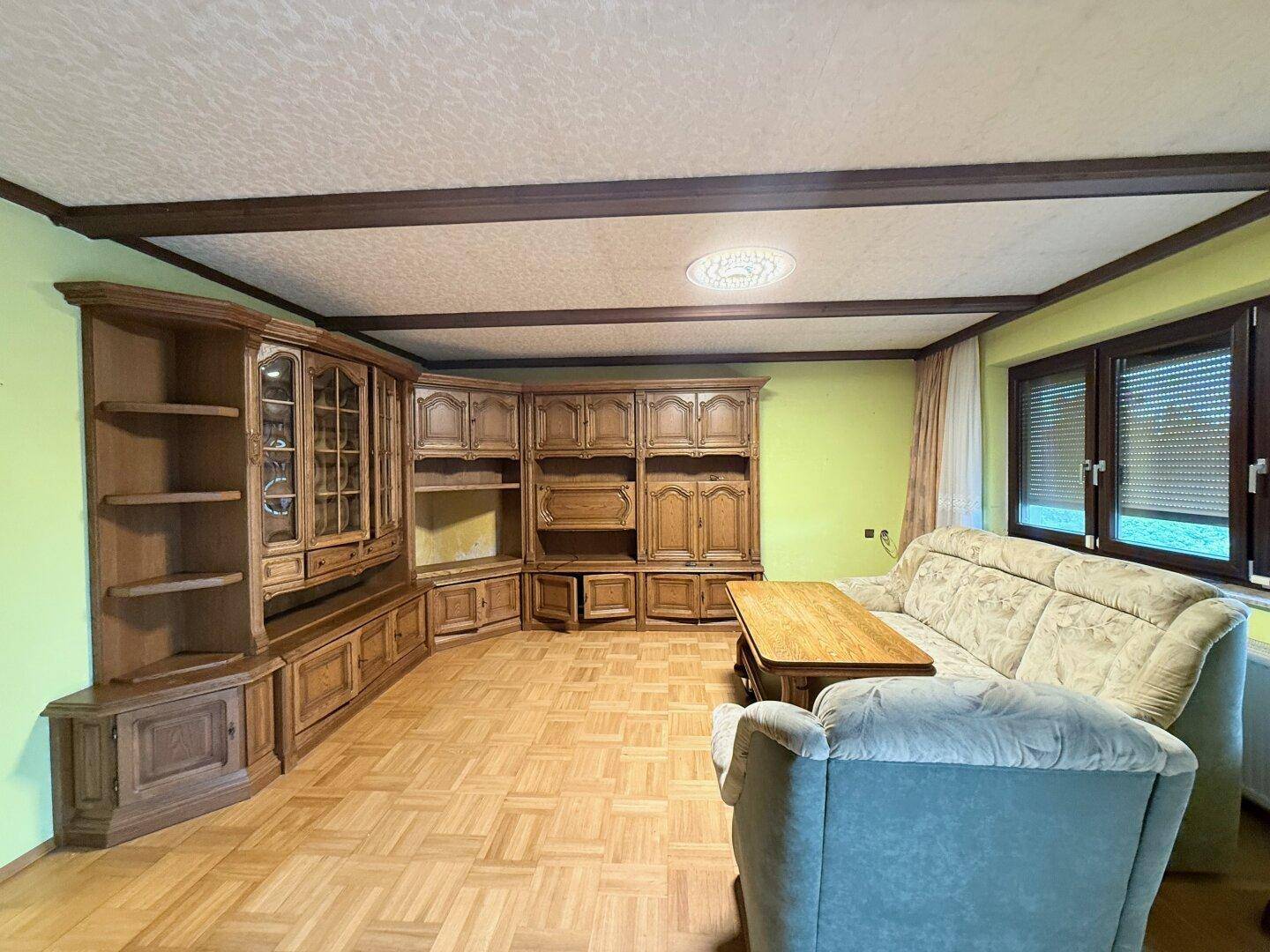 Wohnzimmer mit traditionellen Holzmöbeln, Sofa und gemustertem Parkettboden.