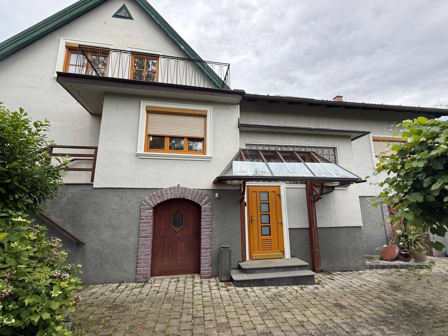 Ansicht des Hauses mit zwei Eingängen, einem kleinen Balkon und gepflastertem Vorplatz.