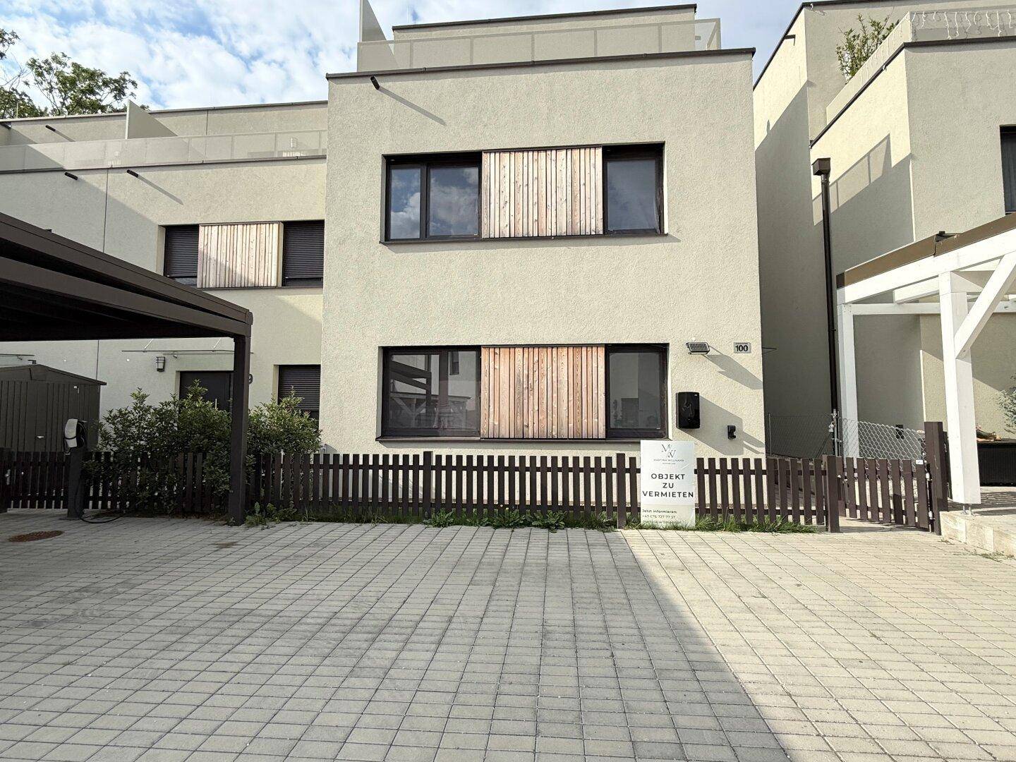 Moderne Reihenhausfassade mit heller Putzfassade, Holzdetails, Carport und gepflasterter Einfahrt.