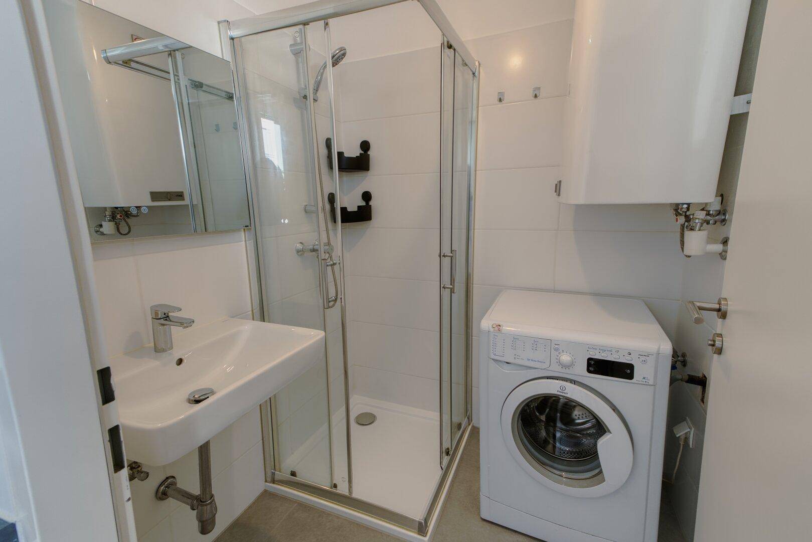 Modernes Badezimmer mit Duschkabine, Waschbecken und integrierter Waschmaschine.