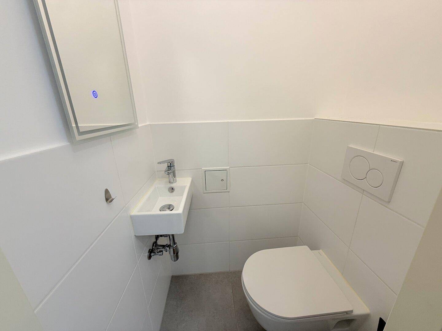 Kleines Gäste-WC mit wandhängender Toilette und modernem Waschbecken in weißer Optik.