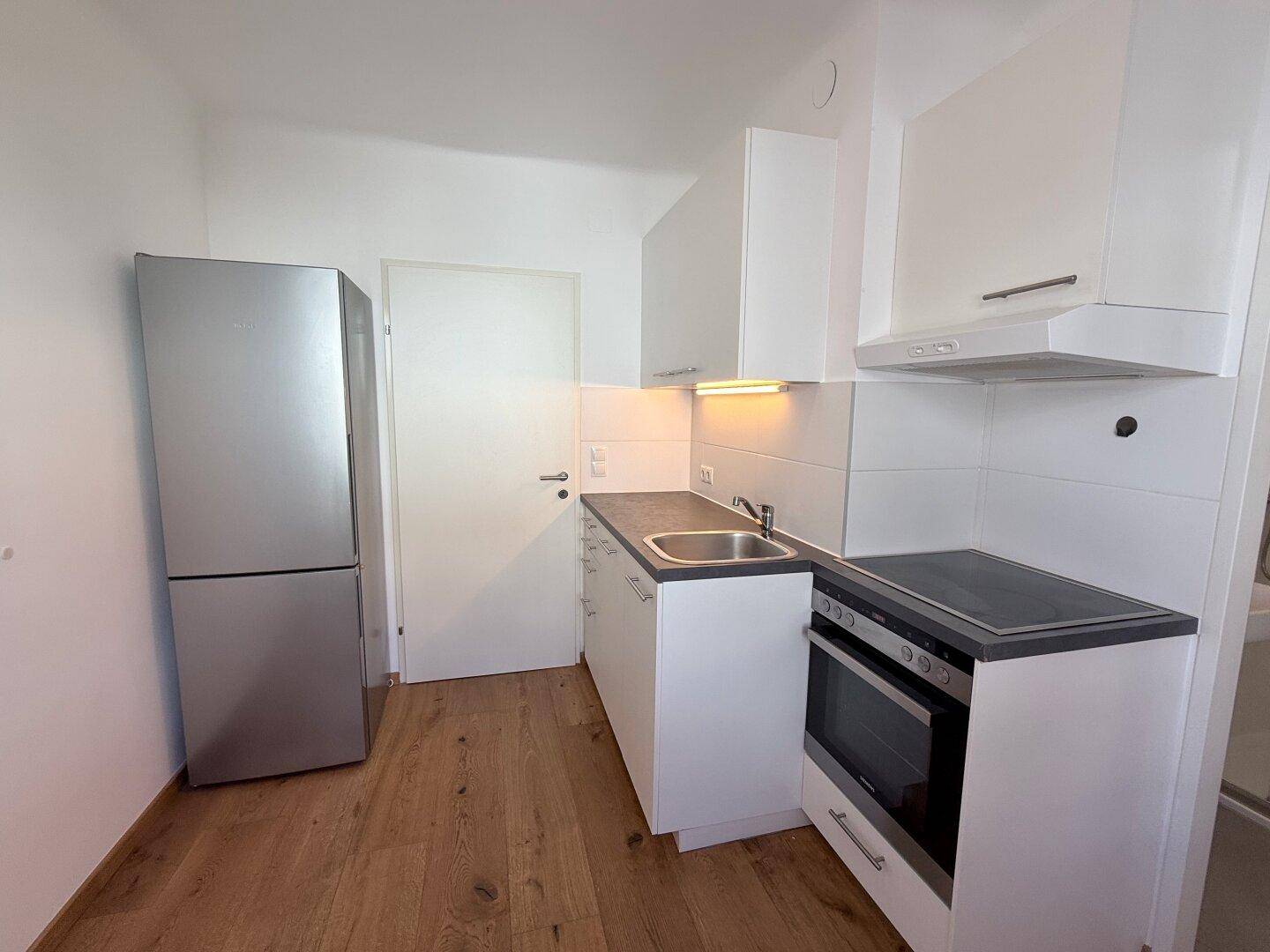 Funktionale Küchenzeile mit Kühlschrank, weißen Schränken und Holzboden in einem hellen Raum.