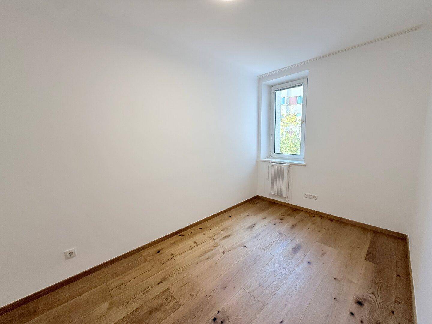Leeres Zimmer mit Holzboden und Fenster, das viel natürliches Licht in den Raum bringt.