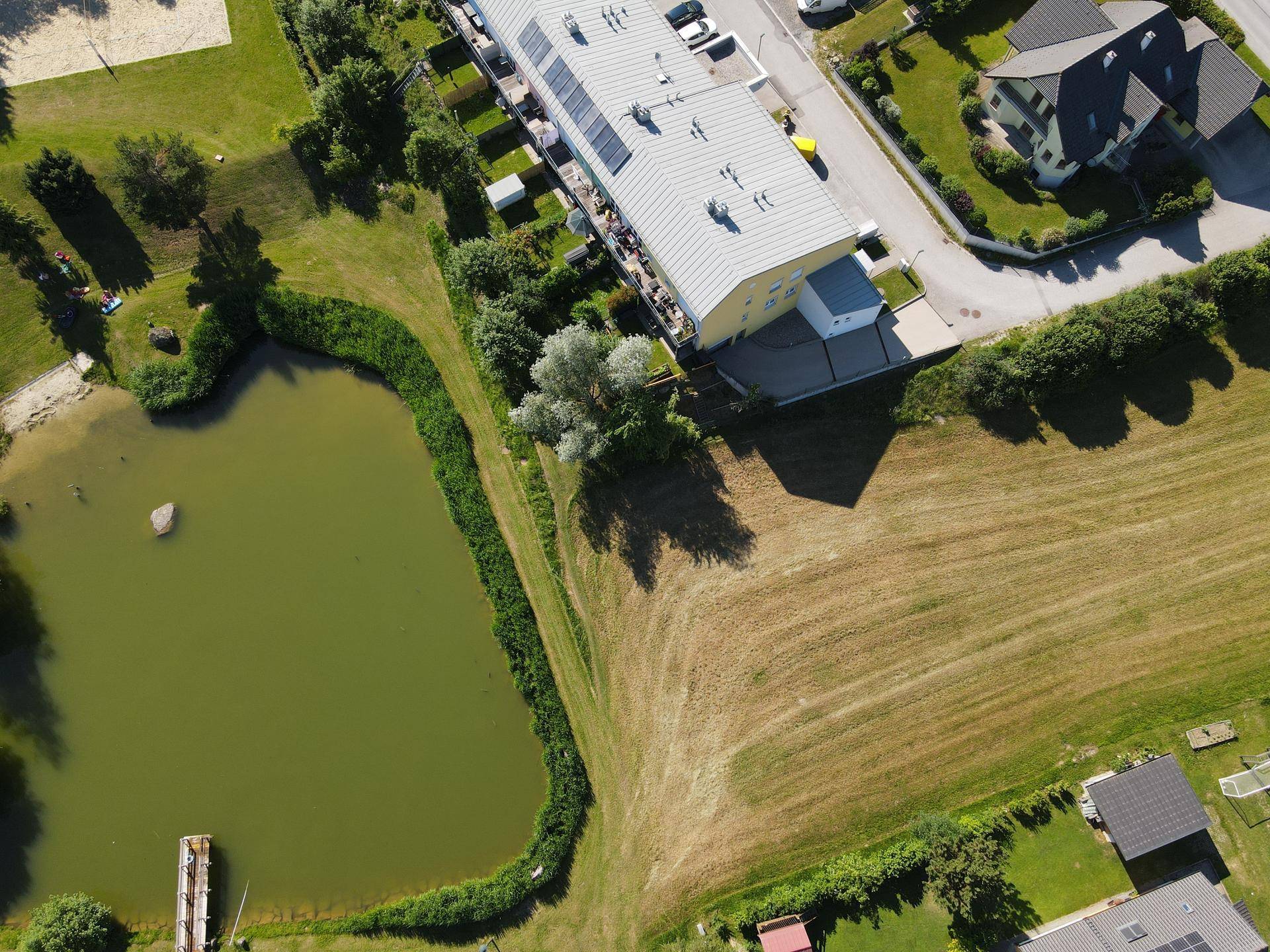 Vogelperspektive auf ein modernes Gebäude neben einem Teich und Feldern in ländlicher Umgebung.