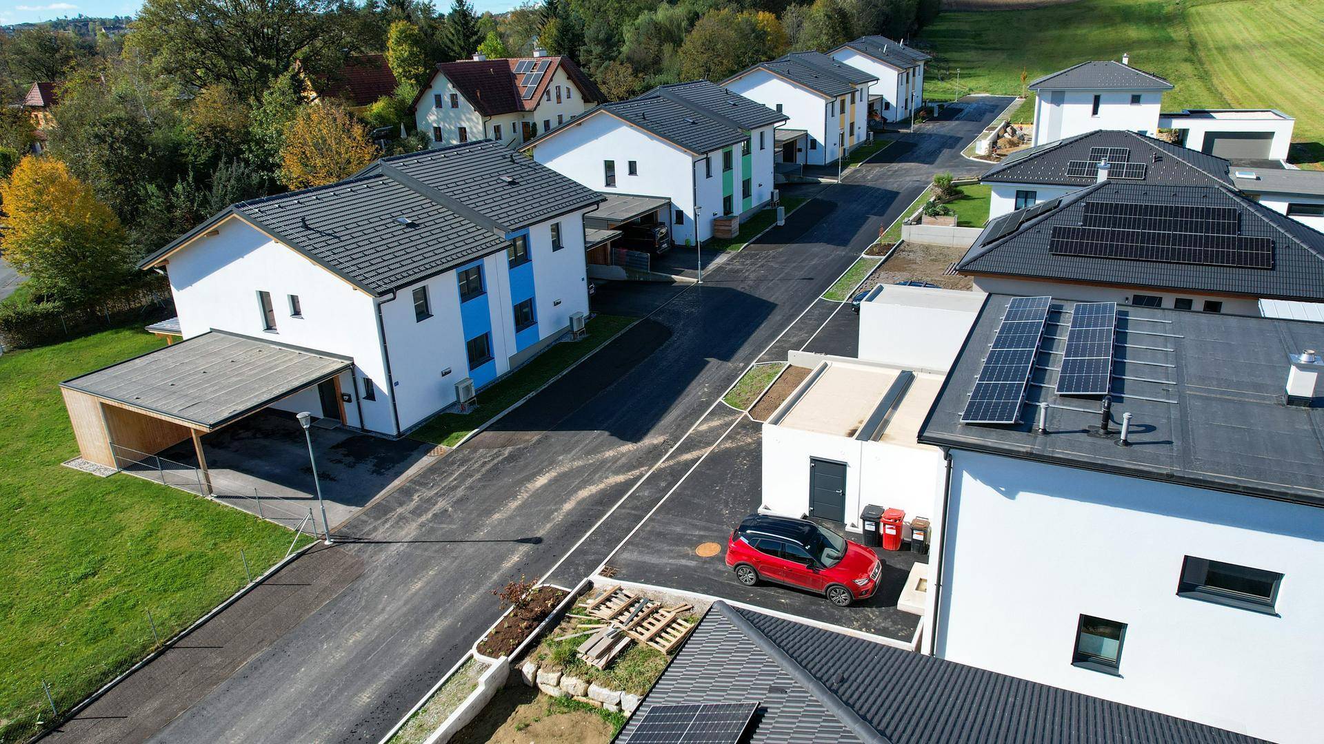 Luftaufnahme einer modernen Wohnsiedlung mit Reihenhäusern, Carports und Solaranlagen auf den Dächern.