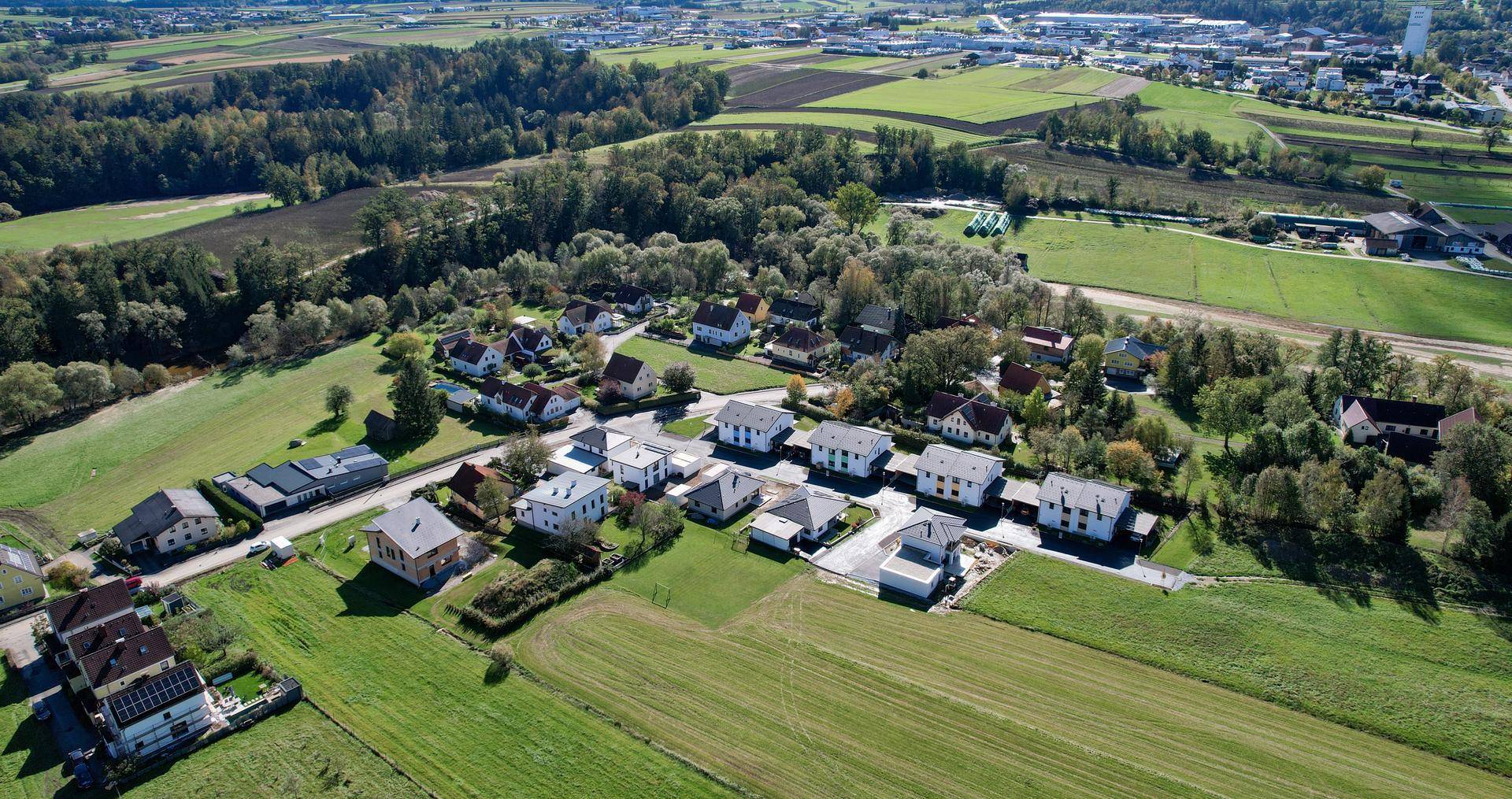 Weitläufige Luftaufnahme einer Wohnsiedlung eingebettet in grüne Felder und Wälder.