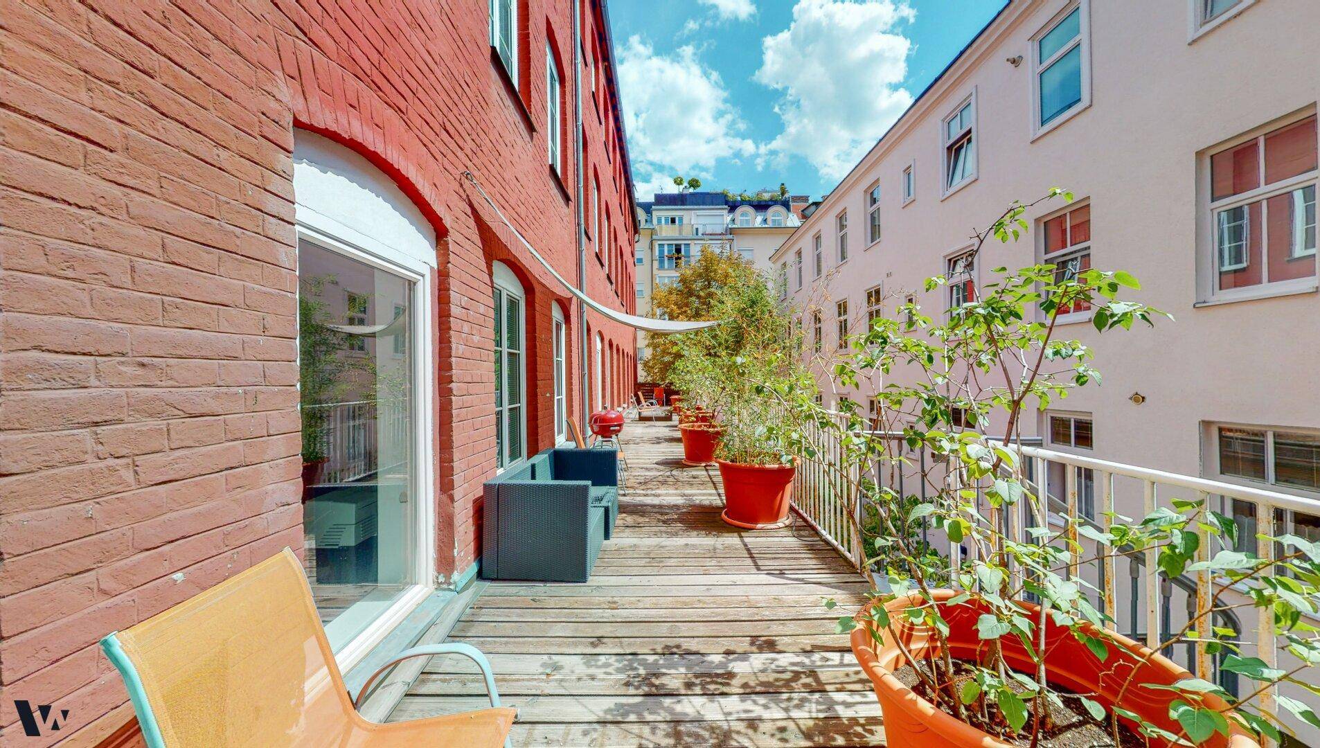 Sonniger Terrassenbereich mit Holzbelag, bequemen Sitzmöbeln und vielen Topfpflanzen.
