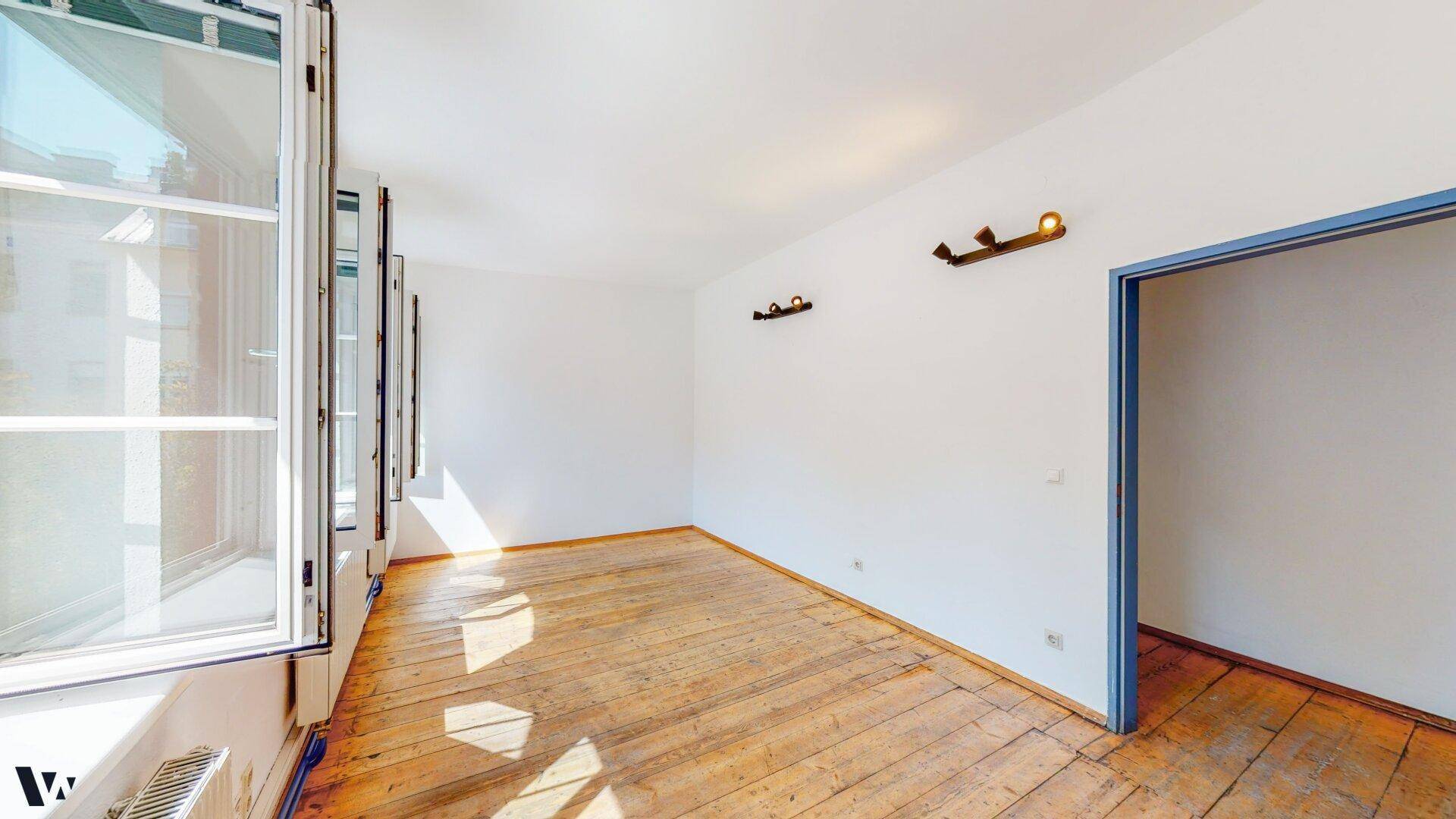 Heller Raum mit Holzdielenboden und mehreren Fenstern, die den Blick nach draußen freigeben.