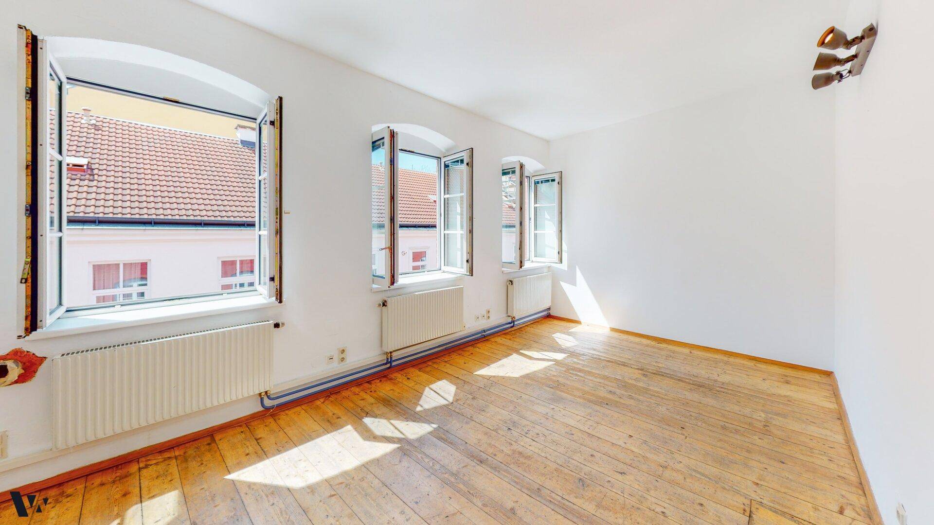 Heller Raum mit Holzdielenboden und drei Fenstern, die viel Tageslicht hereinlassen.