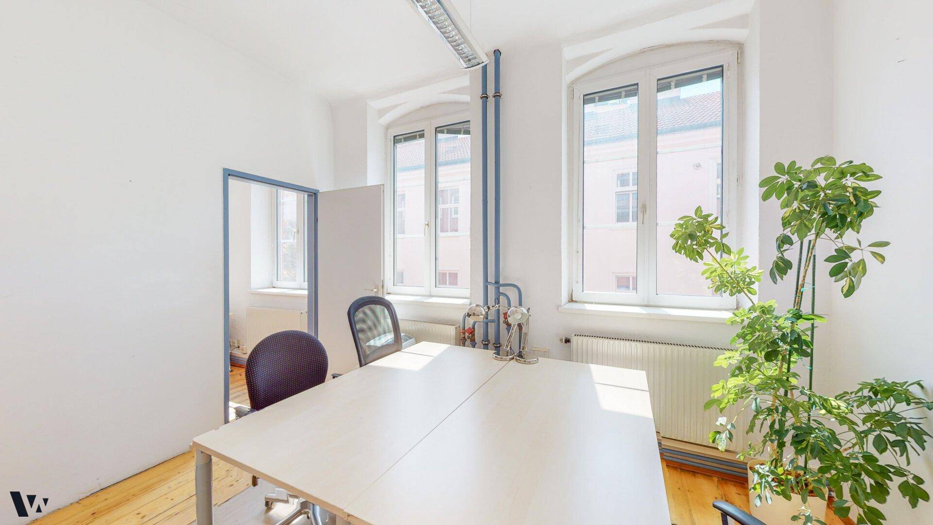 Modernes Büro mit Holzdielenboden, großem Schreibtisch und einer grünen Pflanze.