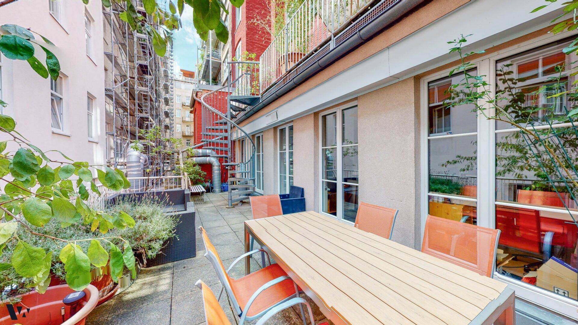 Geräumige Terrasse mit Esstisch, Stühlen und einer Wendeltreppe, umgeben von Pflanzen.